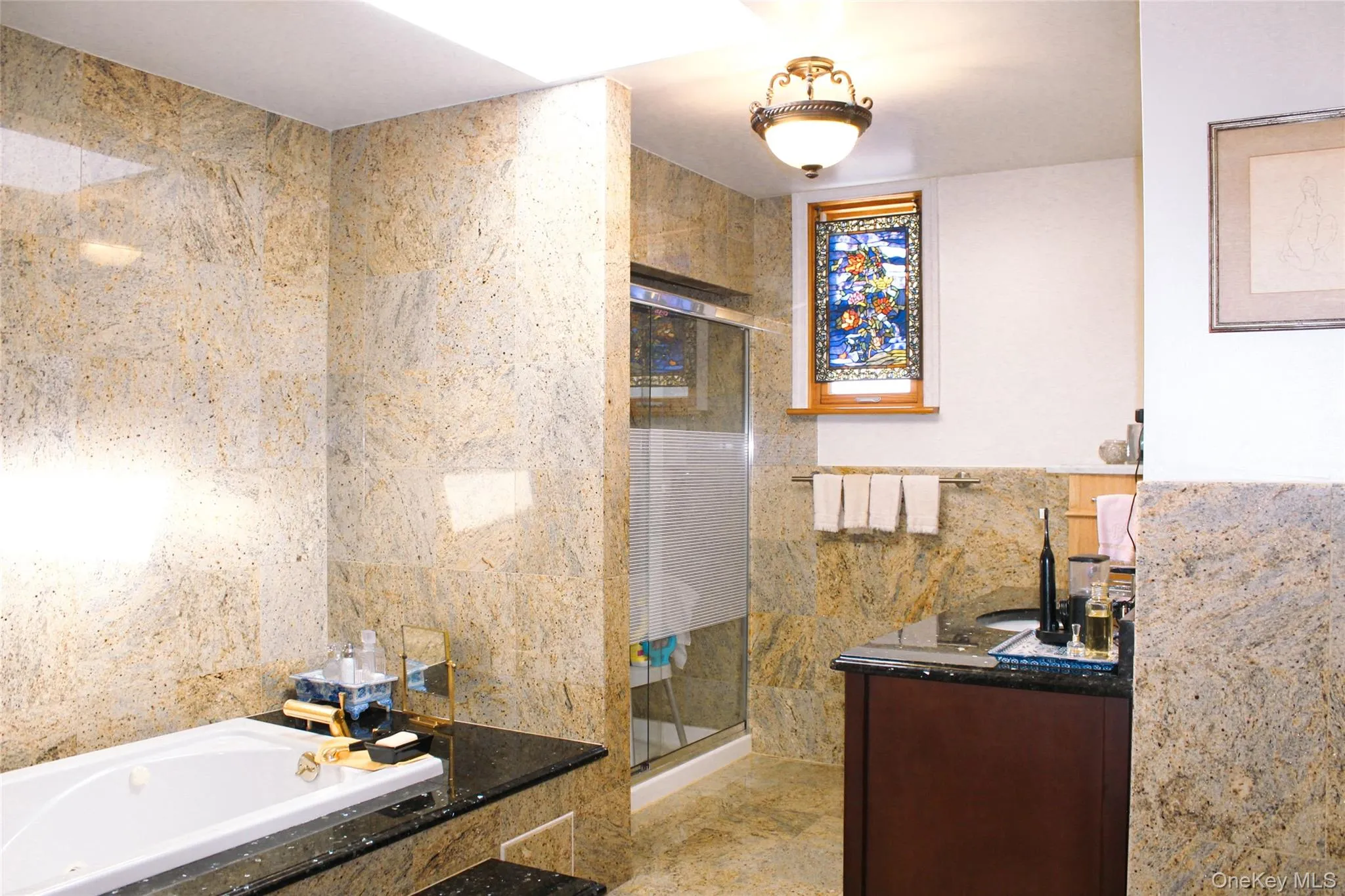 2nd floor bathroom has tiled walls and flooring, built-in bathtub, glass-enclosed shower, stained glass window, and vanity with dark countertop 2nd floor bathroom has tiled walls and flooring, built-in bathtub, glass-enclosed shower, stained glass window, and vanity with dark countertop