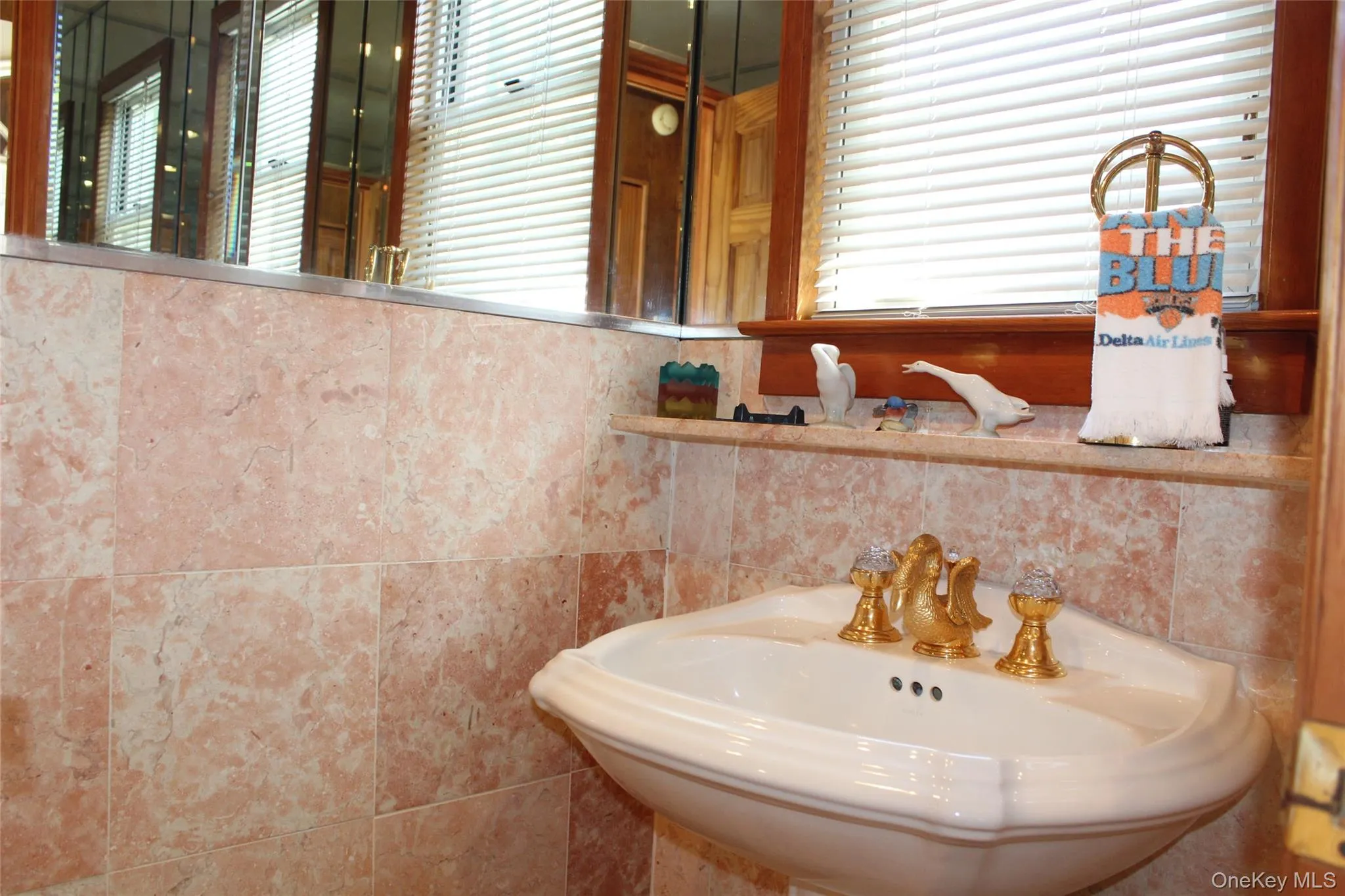 1st floor bathroom with pedestal sink with gold-finish faucet, full-width mirror, and marble tiles. 1st floor bathroom with pedestal sink with gold-finish faucet, full-width mirror, and marble tiles.