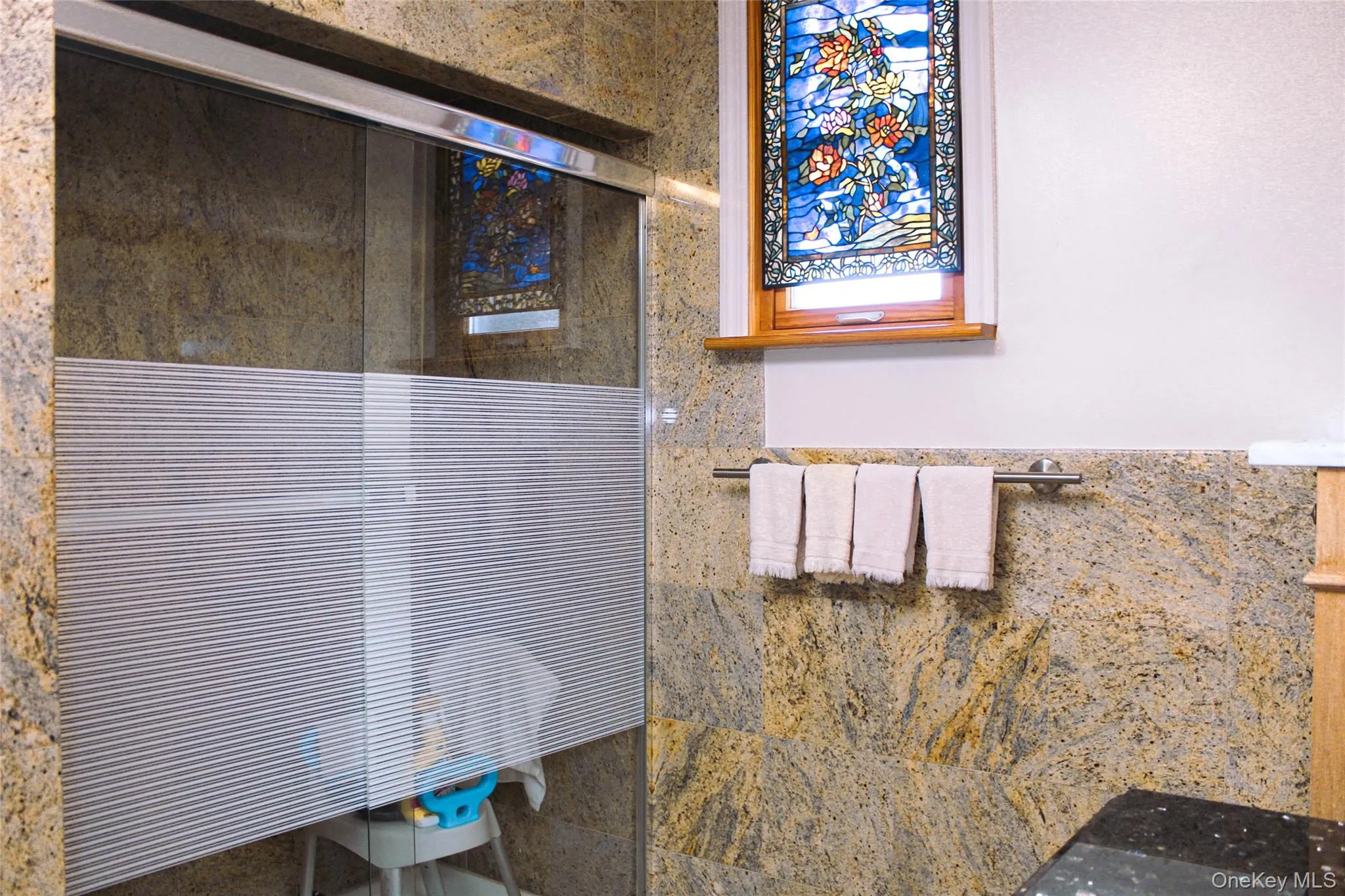 2nd floor bathroom has glass-enclosed shower with frosted panel, natural stone wall finishes, and a stained-glass window accent 2nd floor bathroom has glass-enclosed shower with frosted panel, natural stone wall finishes, and a stained-glass window accent