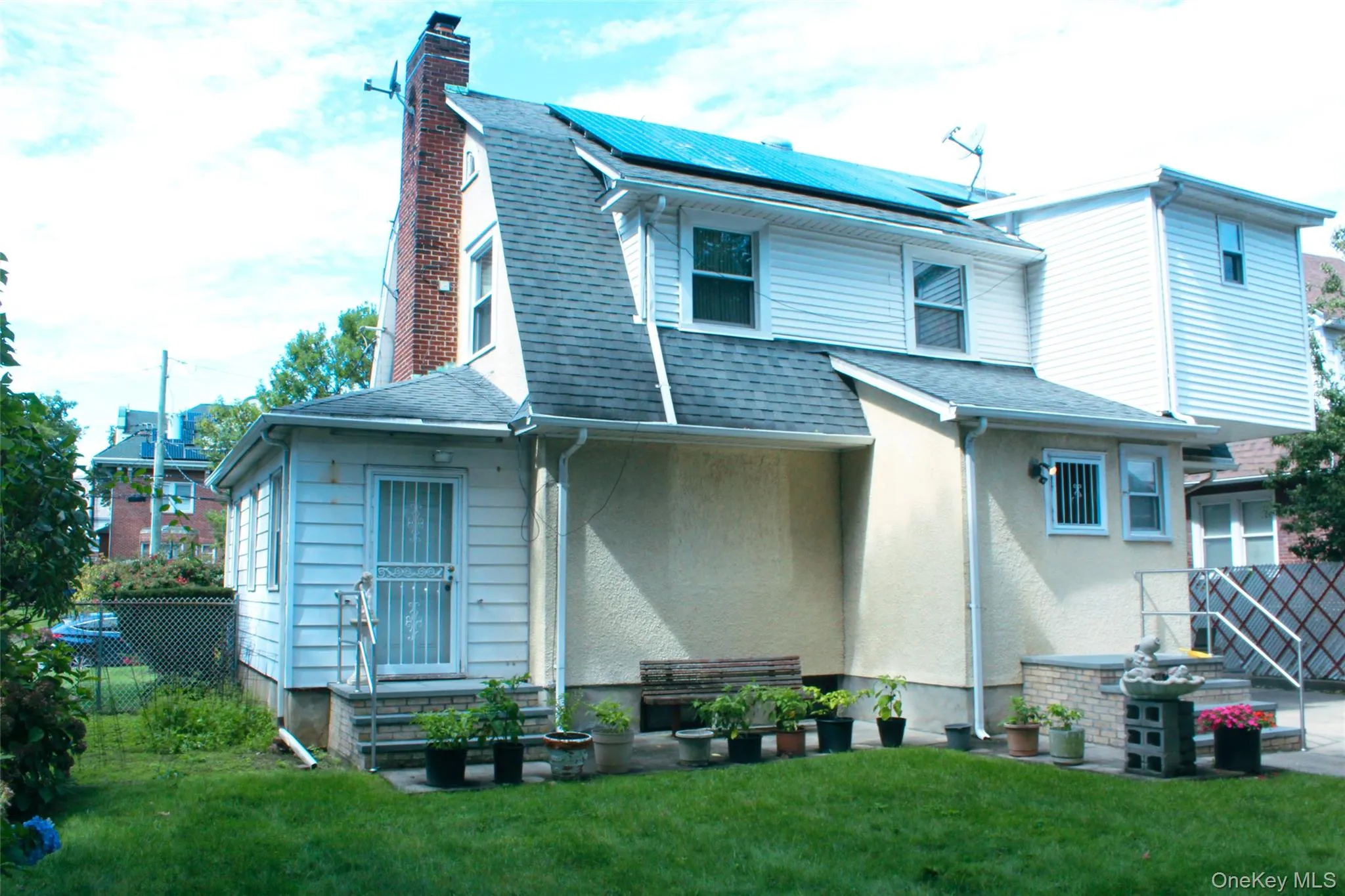 Manicured lawn, brick chimney, multiple windows, solar panels, and a rear entry door Manicured lawn, brick chimney, multiple windows, solar panels, and a rear entry door