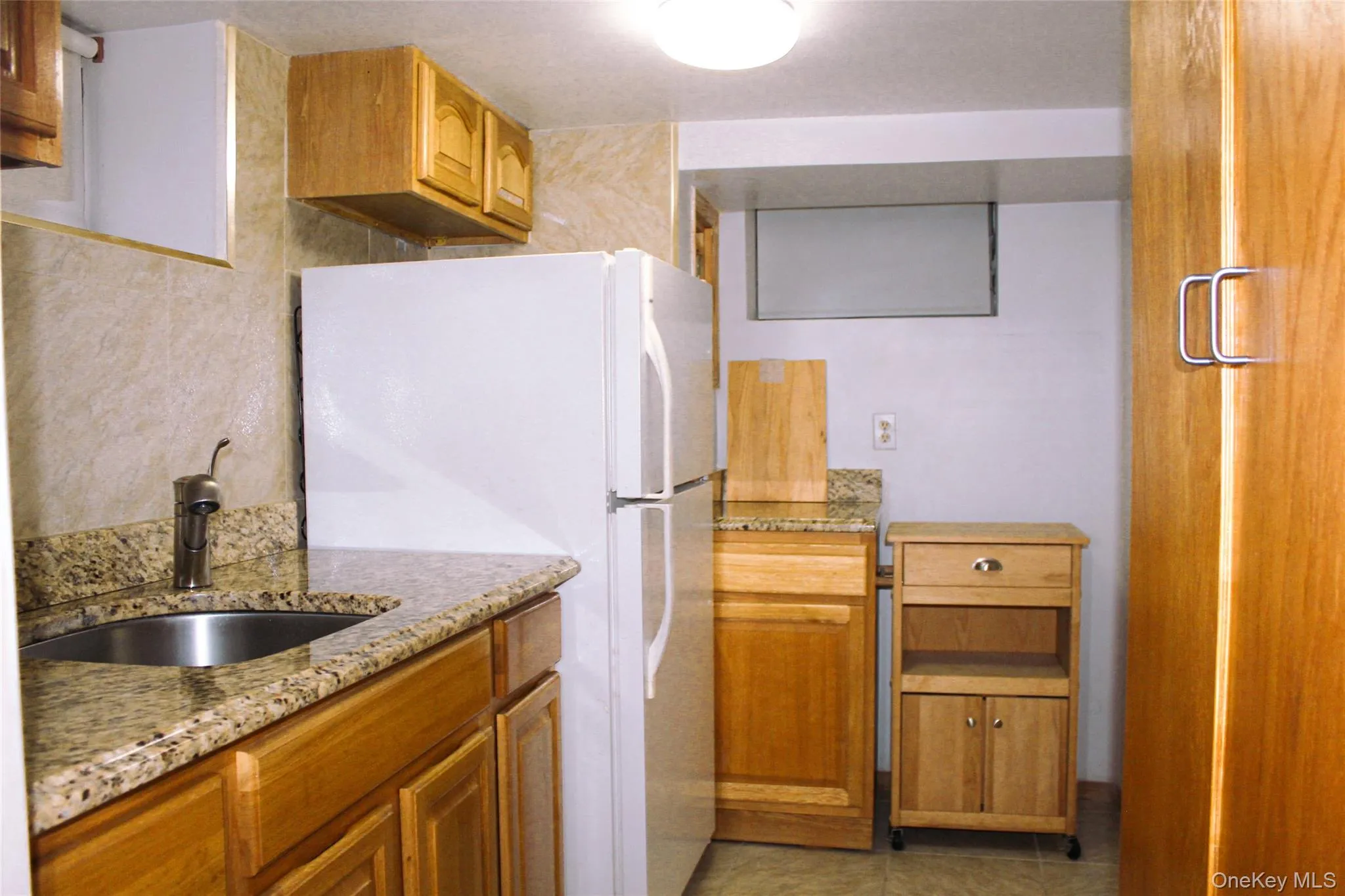 Wood-finish cabinetry with a built-in stainless steel sink, granite-style countertops, and a full-size refrigerator Wood-finish cabinetry with a built-in stainless steel sink, granite-style countertops, and a full-size refrigerator