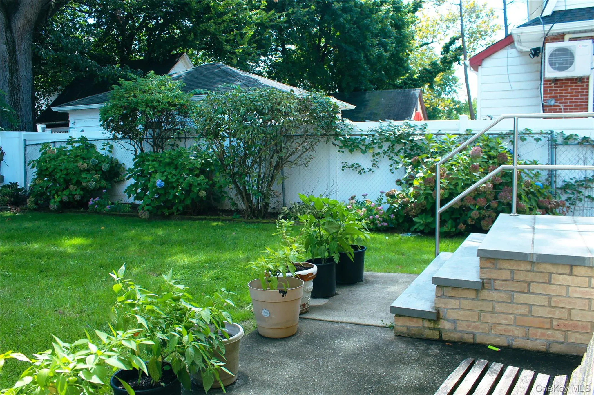 Expansive green lawn, established landscaping, privacy fencing, concrete patio, and brick steps with a metal handrail Expansive green lawn, established landscaping, privacy fencing, concrete patio, and brick steps with a metal handrail