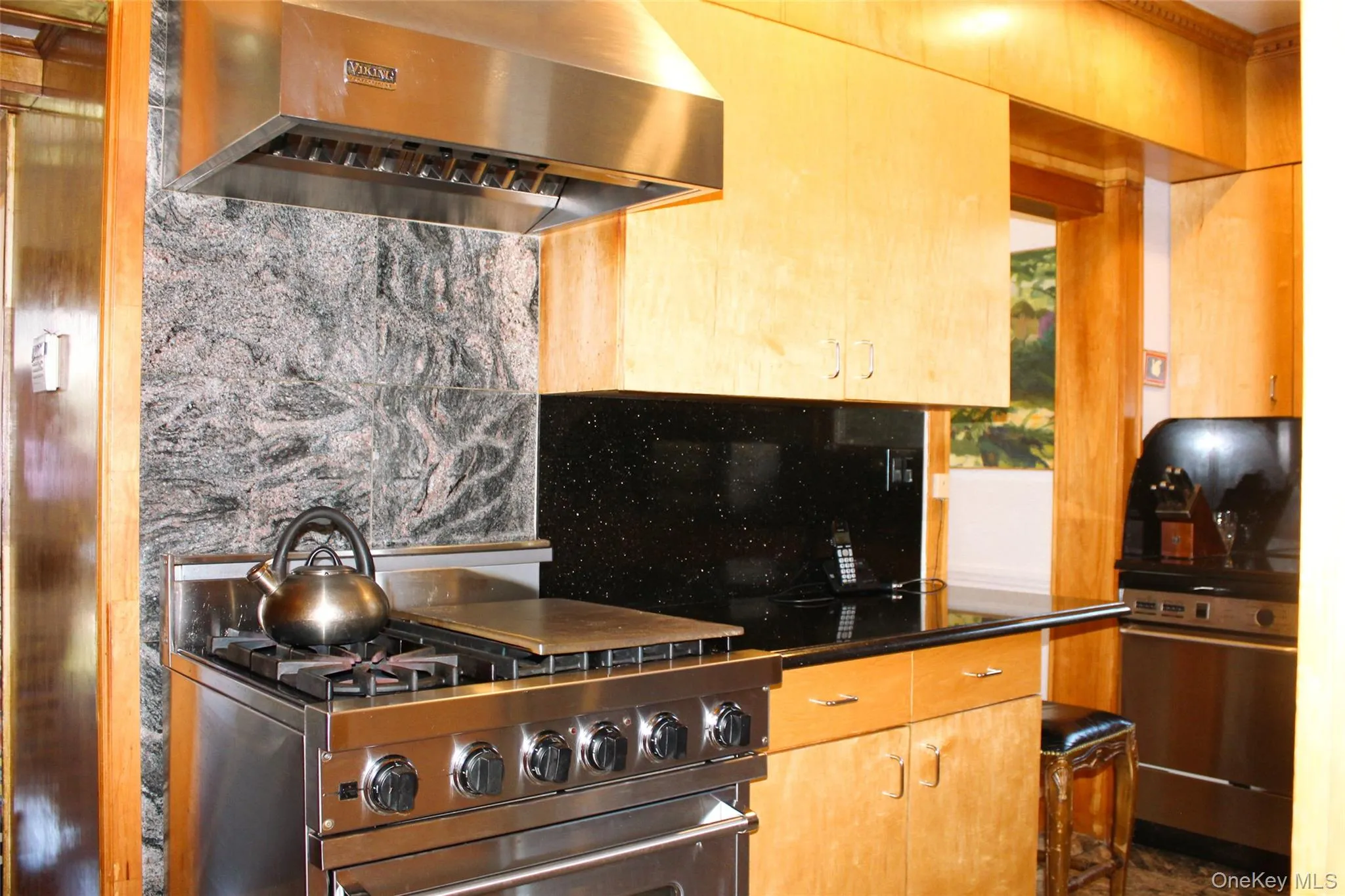 Stainless steel range with a professional-grade hood, natural wood-finish cabinetry, black stone countertops, and a tiled stone backsplash Stainless steel range with a professional-grade hood, natural wood-finish cabinetry, black stone countertops, and a tiled stone backsplash