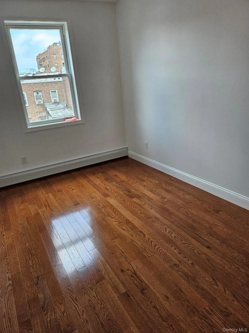Unfurnished room featuring dark wood-style floors and a baseboard radiator Unfurnished room featuring dark wood-style floors and a baseboard radiator