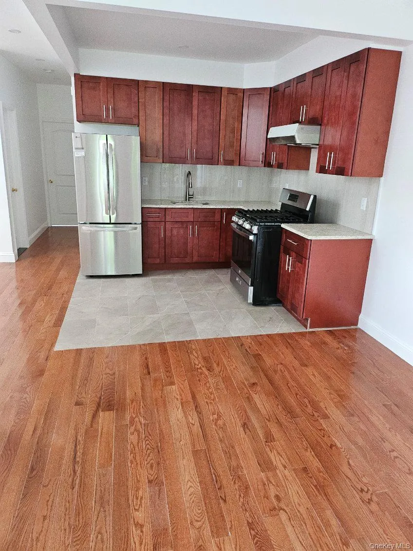 Kitchen featuring appliances with stainless steel finishes, light wood-type flooring, light stone counters, and under cabinet range hood Kitchen featuring appliances with stainless steel finishes, light wood-type flooring, light stone counters, and under cabinet range hood