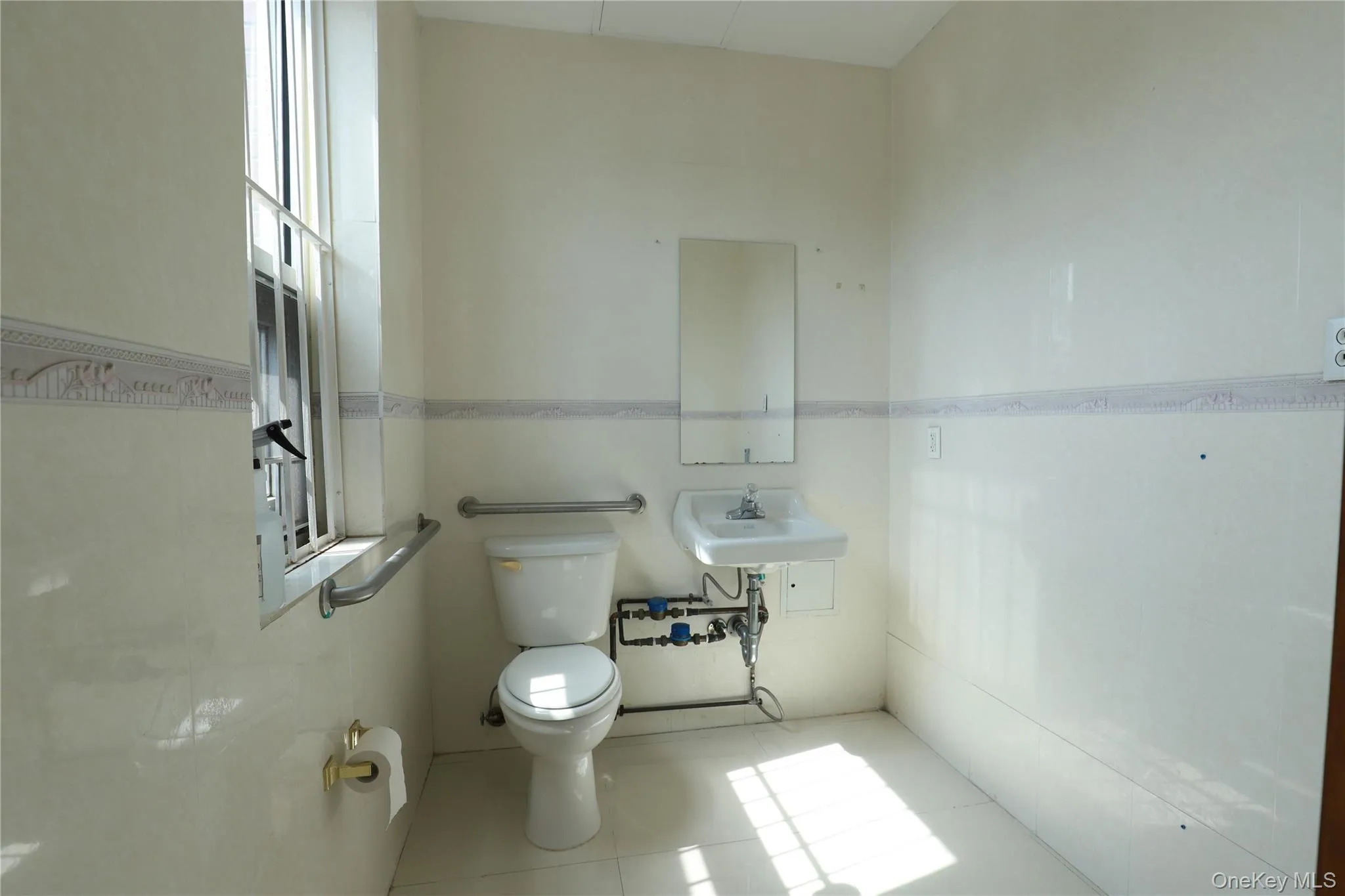 White tile flooring, wall-mounted sink, toilet, window, and grab bars White tile flooring, wall-mounted sink, toilet, window, and grab bars