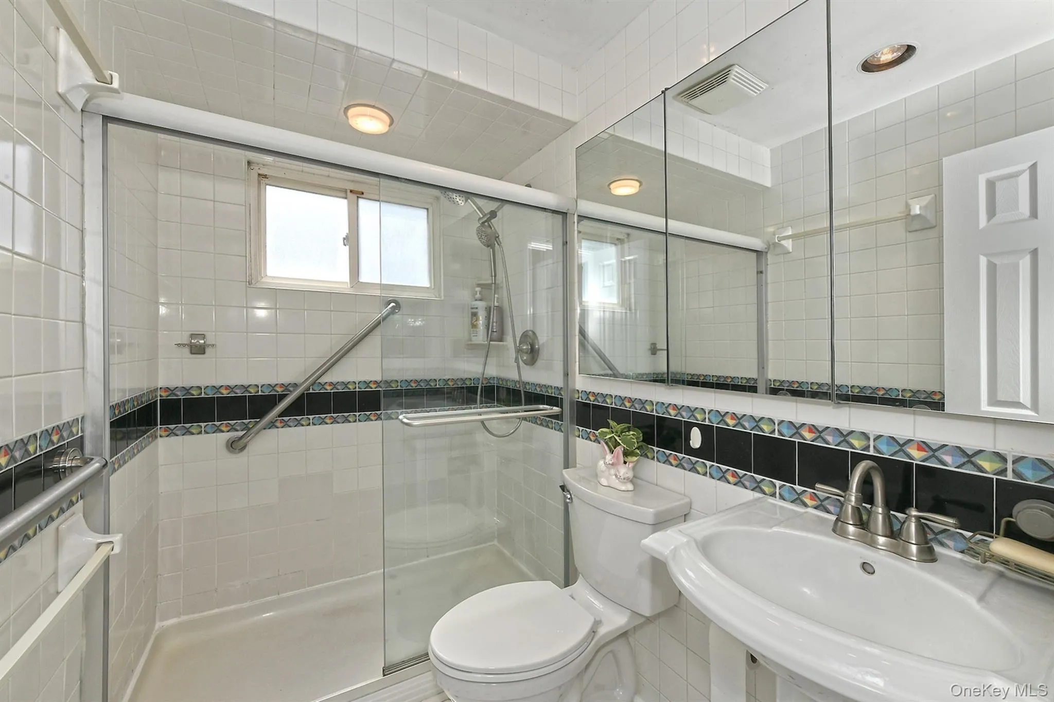 Shower with a clear glass enclosure, white tile surround, and grab bars Shower with a clear glass enclosure, white tile surround, and grab bars