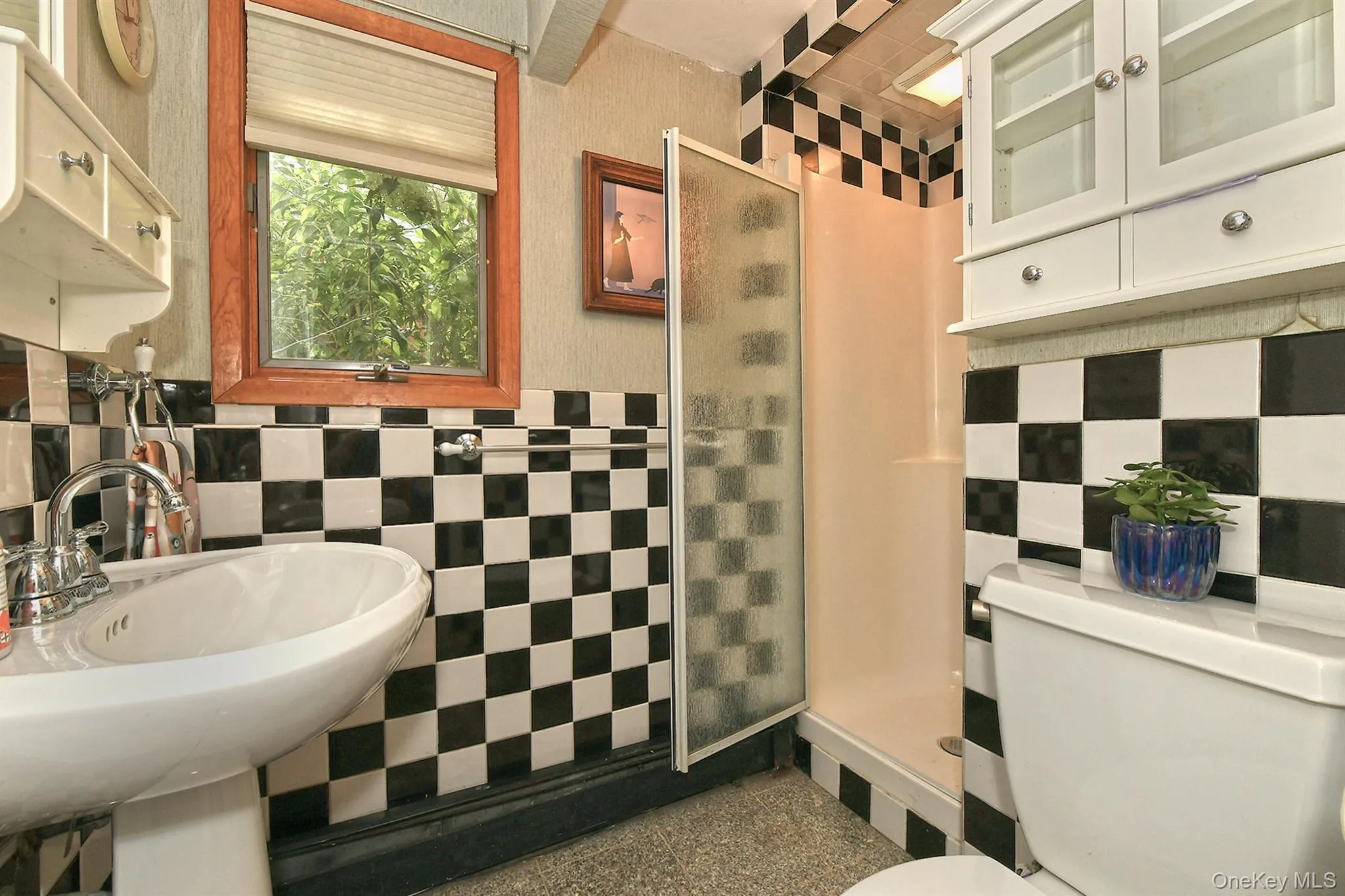 White pedestal sink with chrome faucet, checkerboard wall tile, and a built-in shower stall with an opaque glass door White pedestal sink with chrome faucet, checkerboard wall tile, and a built-in shower stall with an opaque glass door