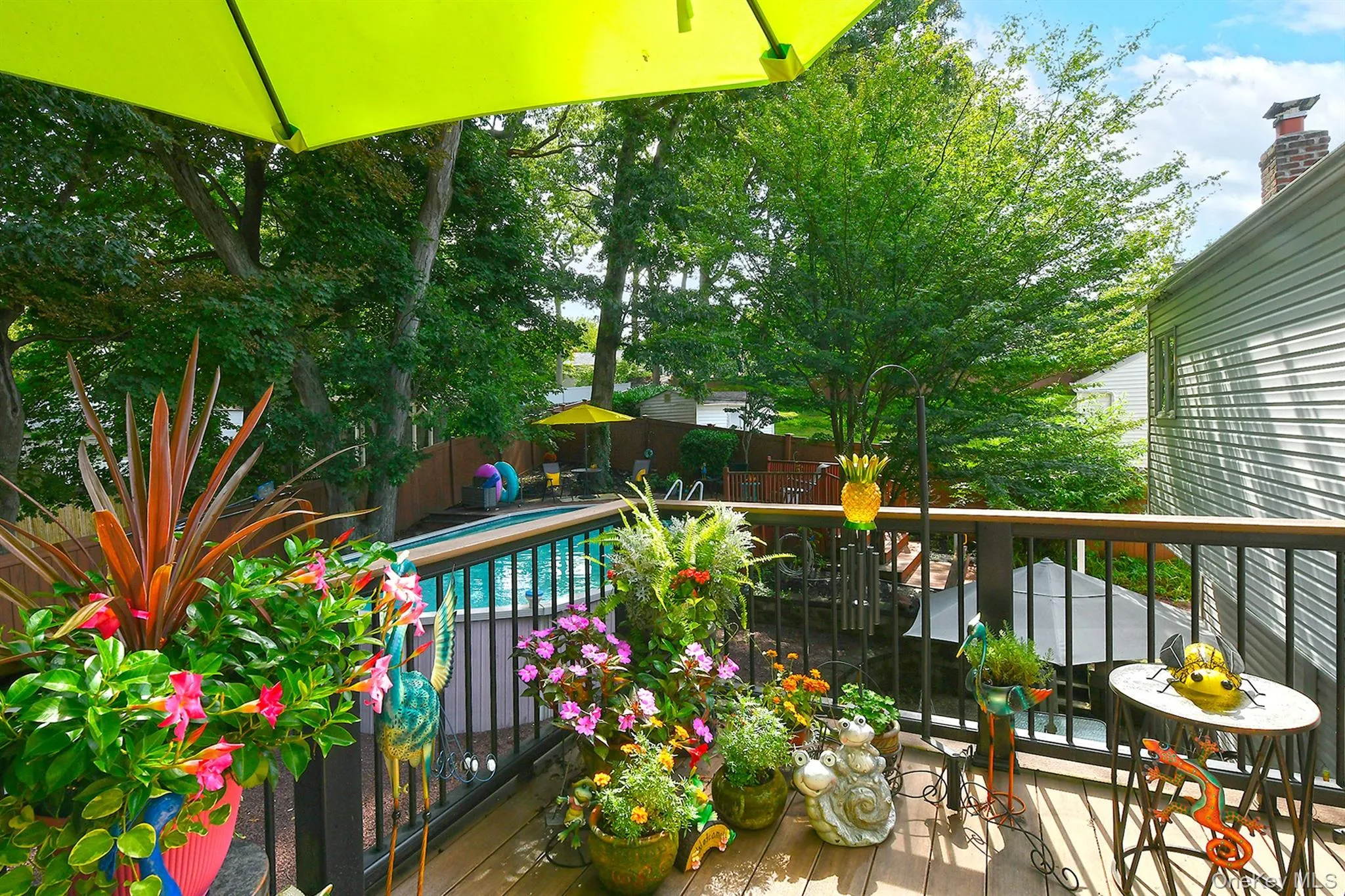 Outdoor deck with wood-finish flooring and black spindle railings, featuring a built-in swimming pool and mature trees Outdoor deck with wood-finish flooring and black spindle railings, featuring a built-in swimming pool and mature trees