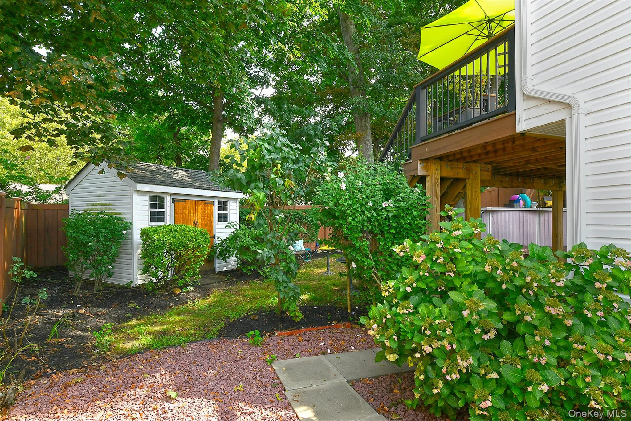 Elevated wood deck with dark railing, white siding exterior, and a detached storage shed with natural wood doors Elevated wood deck with dark railing, white siding exterior, and a detached storage shed with natural wood doors