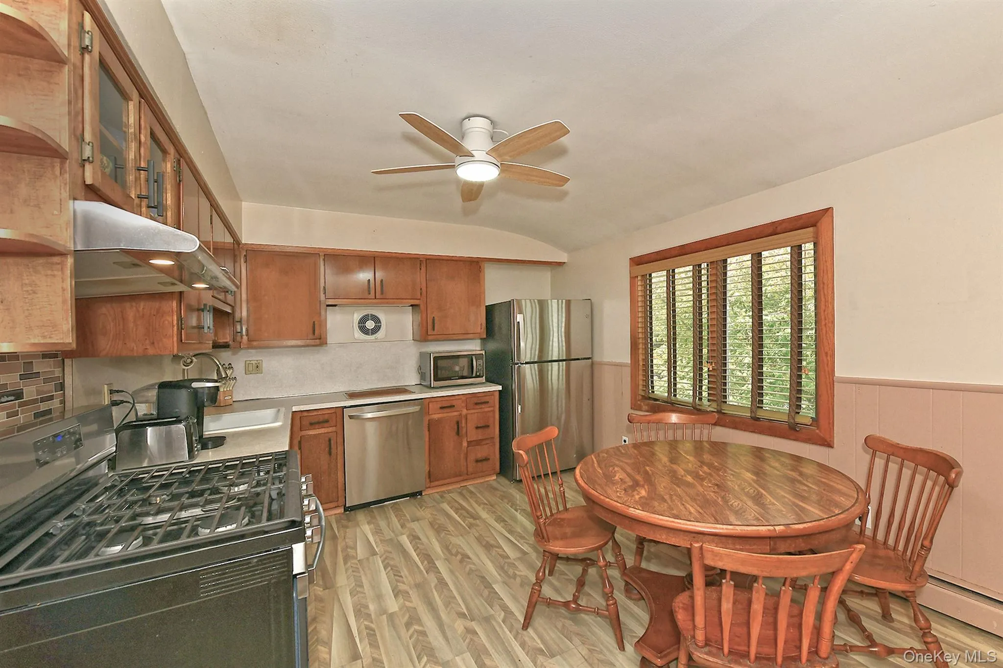 Kitchen featuring wood-finish flooring, wood cabinetry, stainless steel appliances, and a ceiling fan Kitchen featuring wood-finish flooring, wood cabinetry, stainless steel appliances, and a ceiling fan