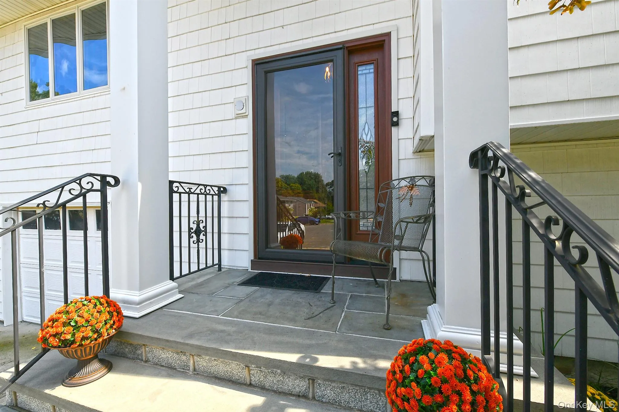 Stone step entry leading to a covered porch with white columns, black wrought iron railings, and a glass-paneled entry door Stone step entry leading to a covered porch with white columns, black wrought iron railings, and a glass-paneled entry door