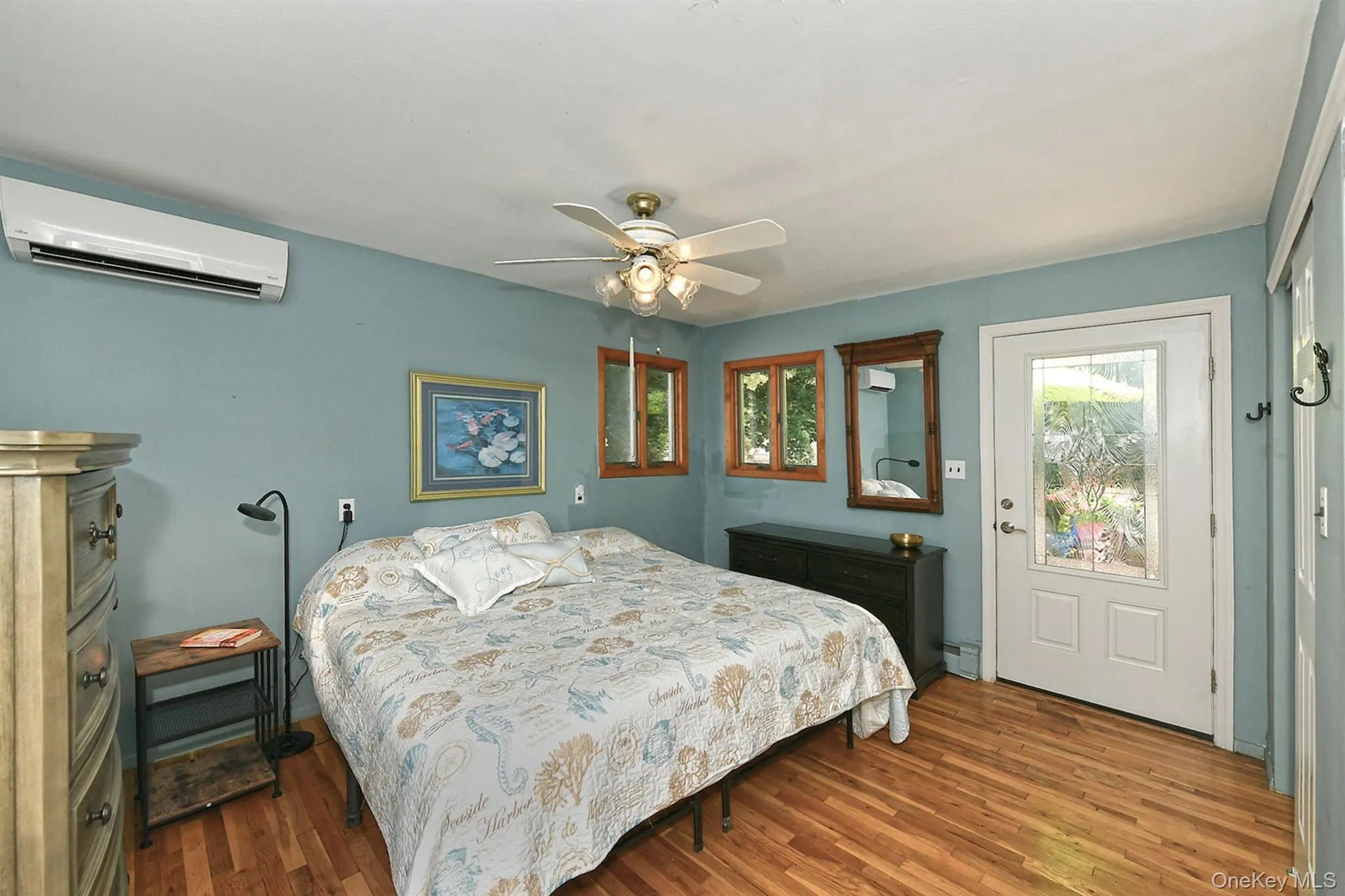 Hardwood flooring with a matte finish, ceiling fan with integrated lighting, wall-mounted air conditioning unit, and a glass-paneled door Hardwood flooring with a matte finish, ceiling fan with integrated lighting, wall-mounted air conditioning unit, and a glass-paneled door
