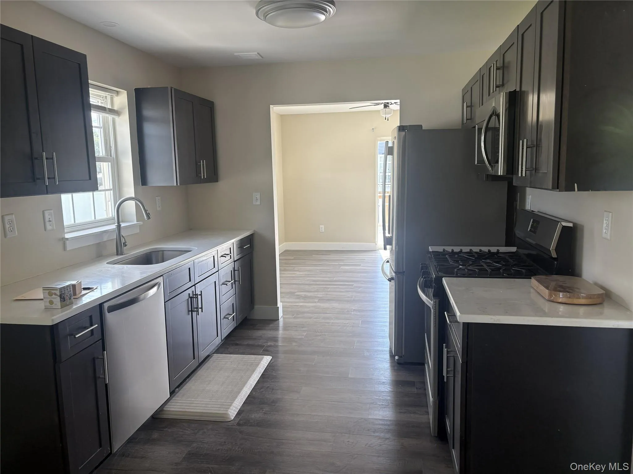 Kitchen featuring dark wood-finish cabinetry, light-toned countertops, stainless steel appliances, and wood-finish flooring Kitchen featuring dark wood-finish cabinetry, light-toned countertops, stainless steel appliances, and wood-finish flooring
