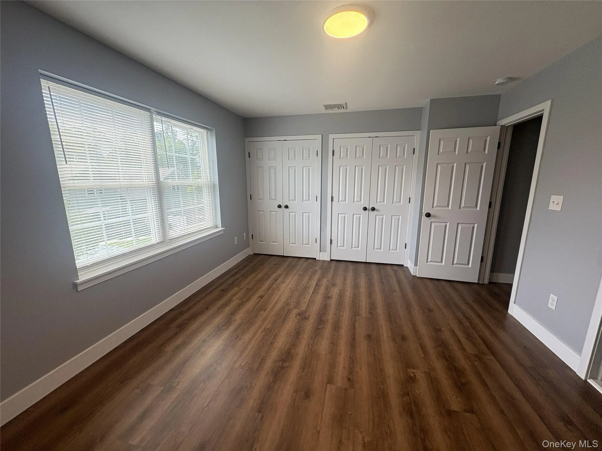 Wood-finish flooring, multiple windows with blinds, two bi-fold closet doors, and a flush mount ceiling light fixture Wood-finish flooring, multiple windows with blinds, two bi-fold closet doors, and a flush mount ceiling light fixture