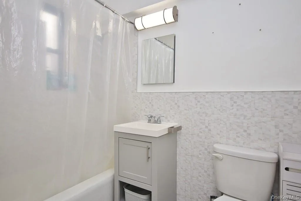 White subway tile bathtub surround, vanity with integrated sink, wall-mounted mirror, and white tiled accent wall White subway tile bathtub surround, vanity with integrated sink, wall-mounted mirror, and white tiled accent wall