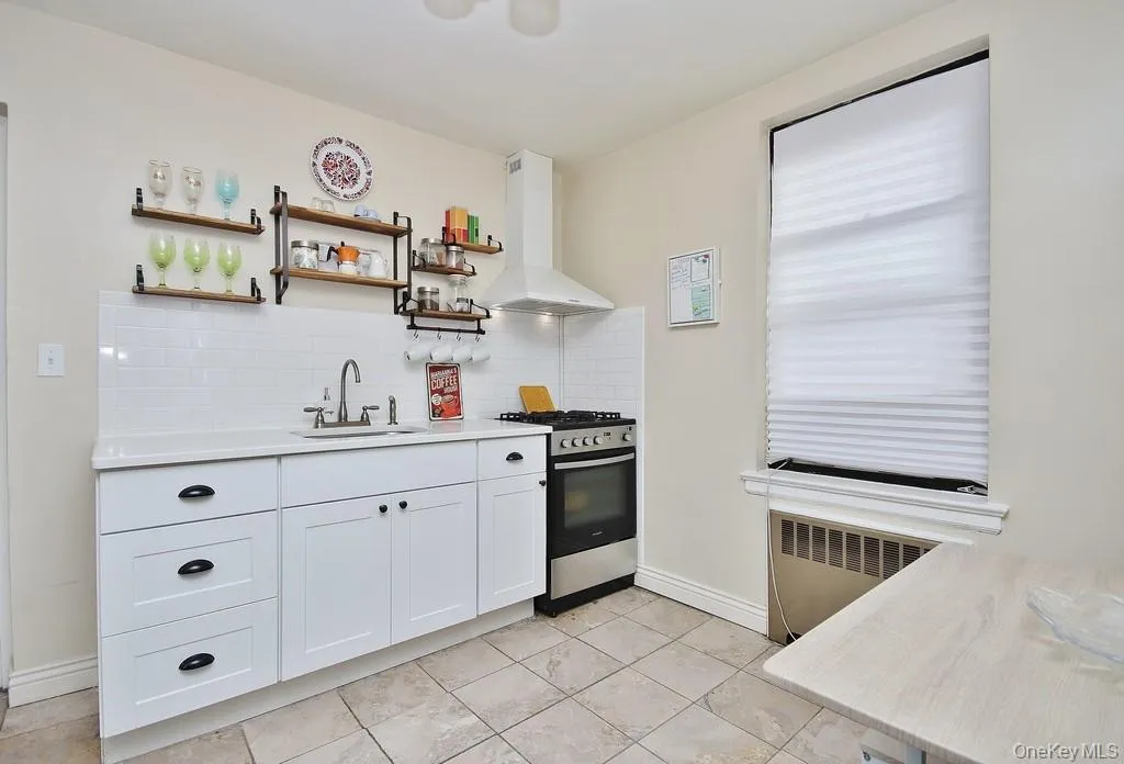 Kitchen featuring white cabinetry with dark hardware, a stainless steel range and matching hood, white subway tile backsplash, and a single basin sink Kitchen featuring white cabinetry with dark hardware, a stainless steel range and matching hood, white subway tile backsplash, and a single basin sink