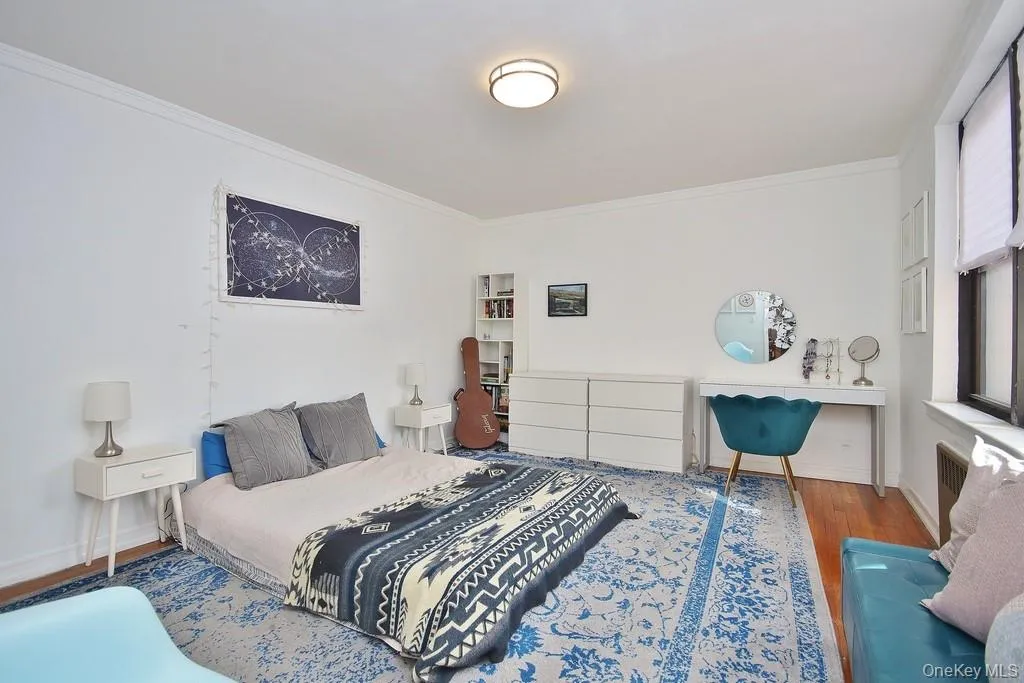 White interior walls, wood-finish flooring, a flush-mount ceiling light fixture, and a window with blinds White interior walls, wood-finish flooring, a flush-mount ceiling light fixture, and a window with blinds
