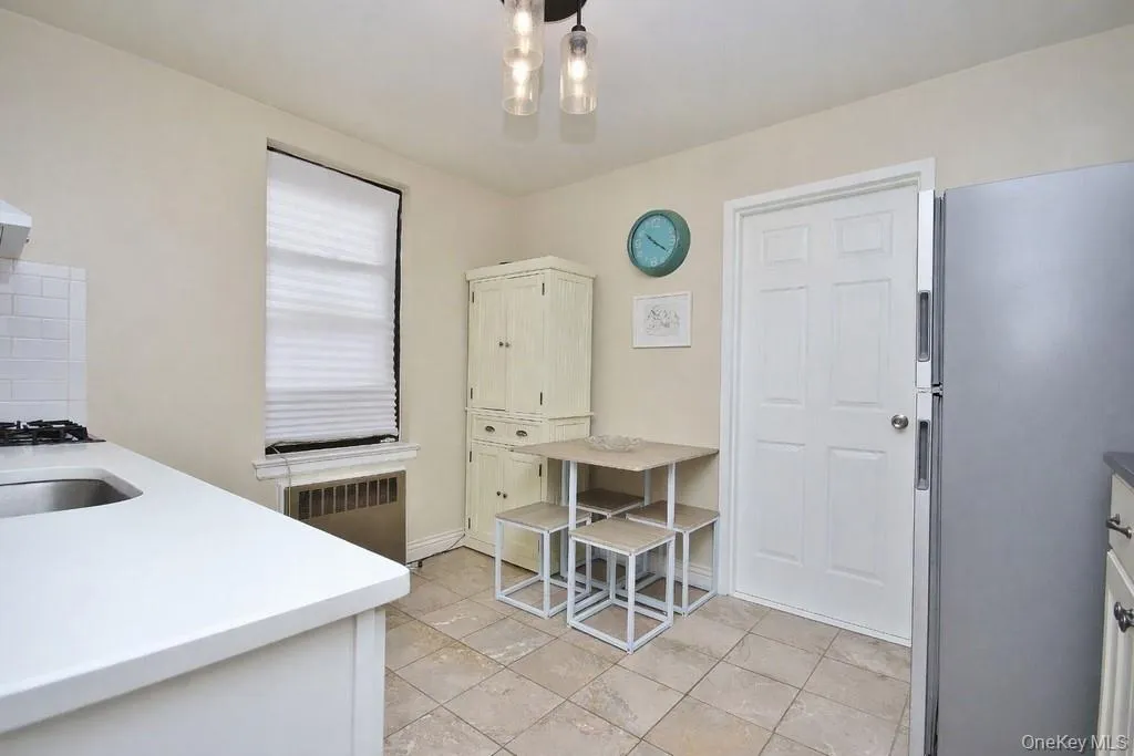 Kitchen featuring neutral-toned tile flooring, light-colored countertops, subway tile backsplash, and a modern ceiling light fixture Kitchen featuring neutral-toned tile flooring, light-colored countertops, subway tile backsplash, and a modern ceiling light fixture