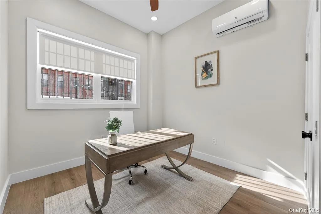Wood-finish flooring, white trim, recessed ceiling lighting, window with roller shades, and a wall-mounted air conditioning unit Wood-finish flooring, white trim, recessed ceiling lighting, window with roller shades, and a wall-mounted air conditioning unit