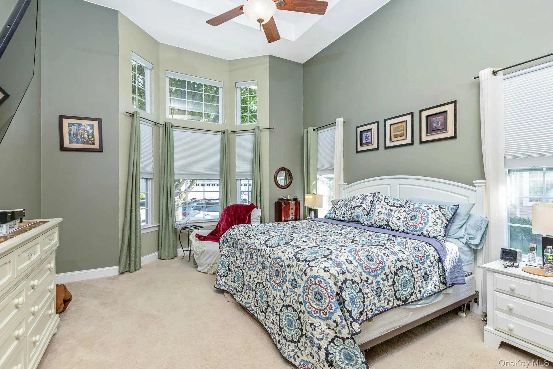 Serene primary bedroom with soft sage-green walls, ceiling fan, and abundant natural light from multi-pane windows Serene primary bedroom with soft sage-green walls, ceiling fan, and abundant natural light from multi-pane windows