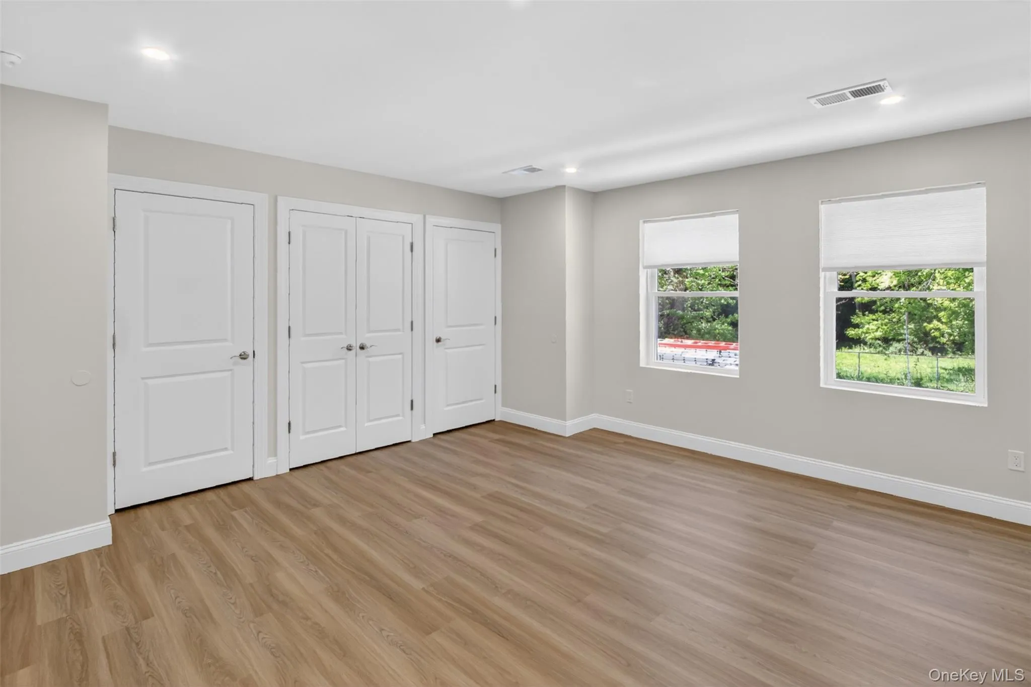 Spacious room featuring wood-finish flooring, light grey wall paint, recessed lighting, and multiple windows with white blinds Spacious room featuring wood-finish flooring, light grey wall paint, recessed lighting, and multiple windows with white blinds