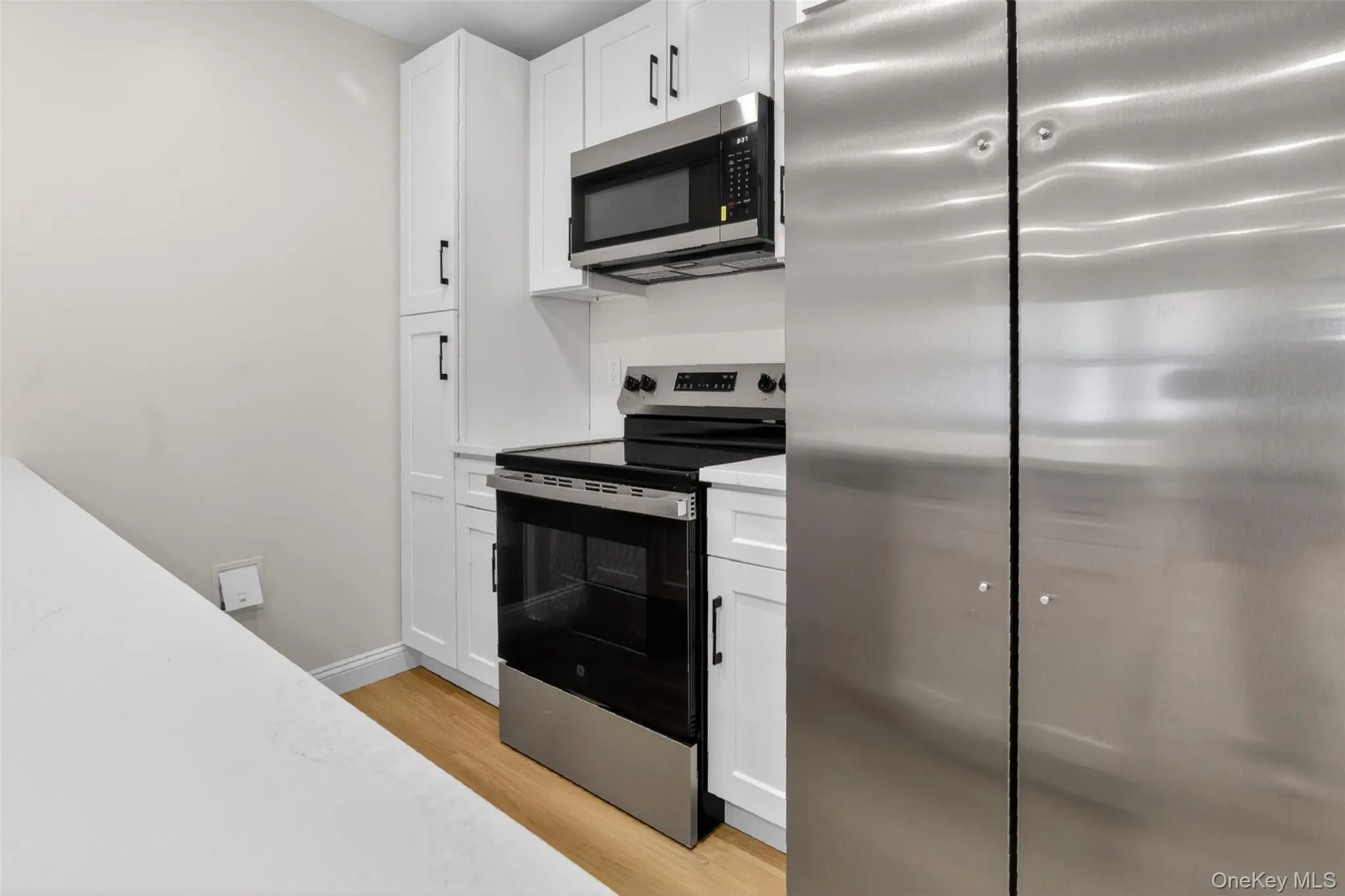 Modern kitchen featuring white cabinetry, stainless steel appliances, light wood-finish flooring, and white countertops Modern kitchen featuring white cabinetry, stainless steel appliances, light wood-finish flooring, and white countertops