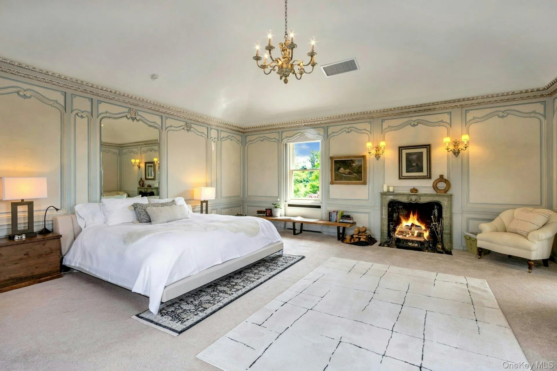 Bedroom with a decorative wall, light colored carpet, a chandelier, and a warm lit fireplace Bedroom with a decorative wall, light colored carpet, a chandelier, and a warm lit fireplace