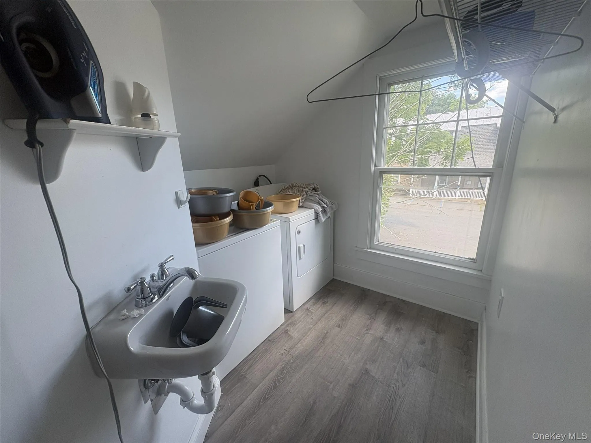 Wall-mounted utility sink, white shelving, wood-finish flooring, and a single window Wall-mounted utility sink, white shelving, wood-finish flooring, and a single window