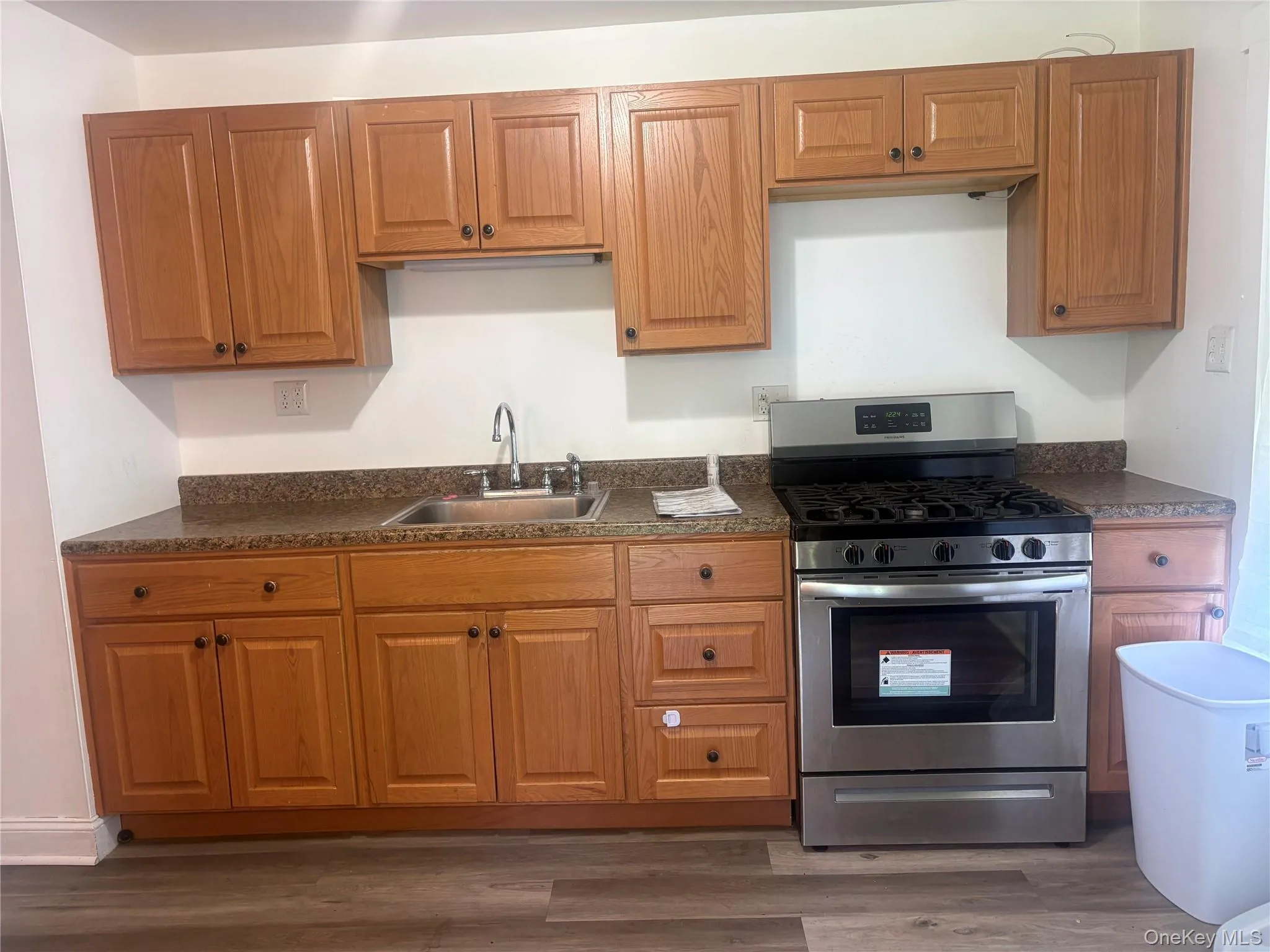 Wood-finish cabinetry with dark hardware, stainless steel range with gas cooktop, double basin sink with chrome faucet, laminate countertops, and wood-finish flooring Wood-finish cabinetry with dark hardware, stainless steel range with gas cooktop, double basin sink with chrome faucet, laminate countertops, and wood-finish flooring