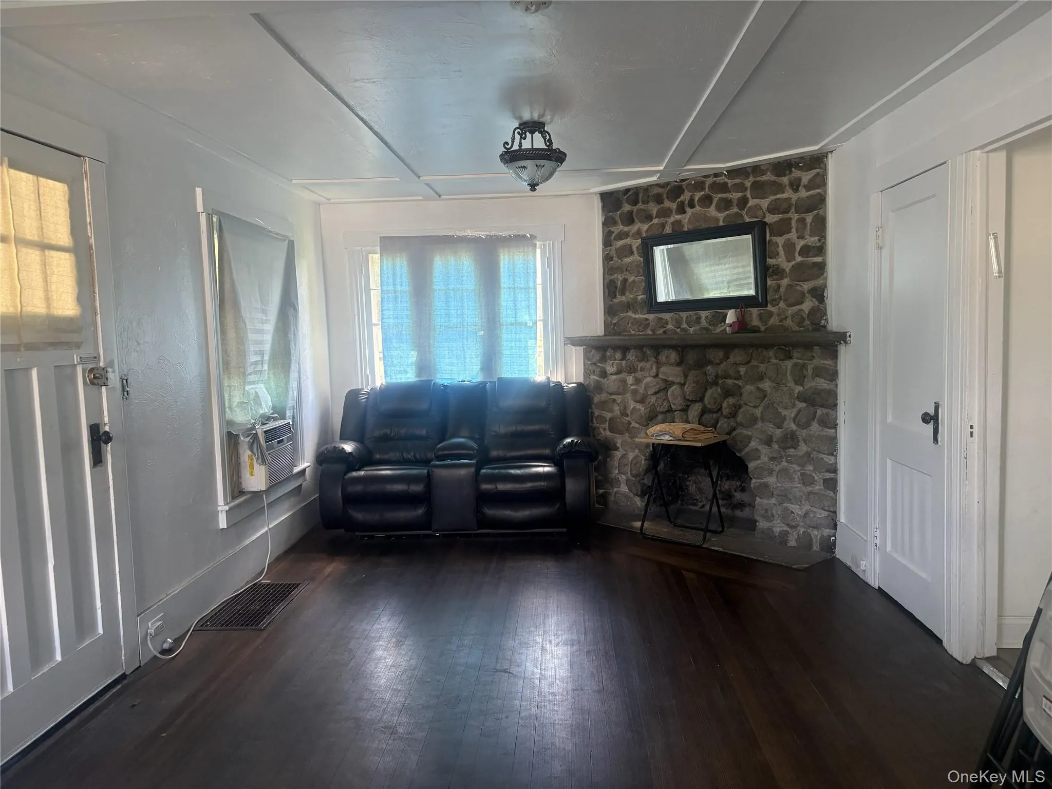 Stone-clad fireplace with a substantial mantel, dark wood-finish flooring, white paneled doors, and a decorative ceiling fixture Stone-clad fireplace with a substantial mantel, dark wood-finish flooring, white paneled doors, and a decorative ceiling fixture