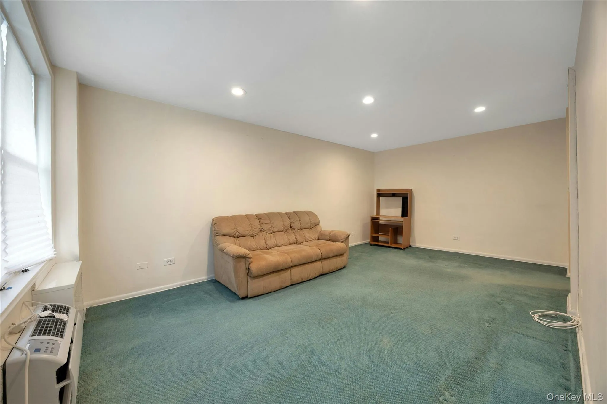 Spacious room featuring light-toned walls, recessed ceiling lighting, and blue-green carpeting Spacious room featuring light-toned walls, recessed ceiling lighting, and blue-green carpeting