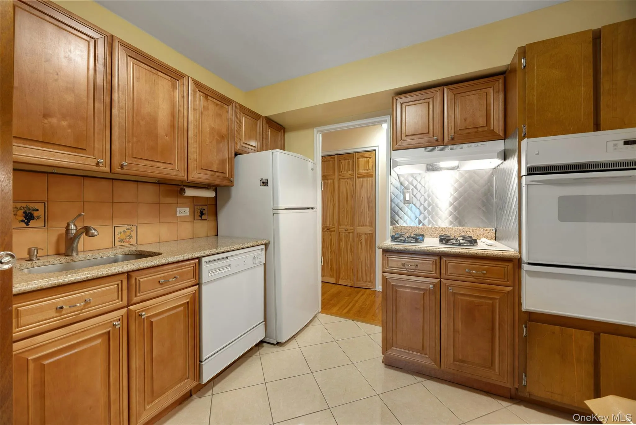 Kitchen featuring wood cabinetry, stone countertops, a tile backsplash, and a ceramic tile floor Kitchen featuring wood cabinetry, stone countertops, a tile backsplash, and a ceramic tile floor