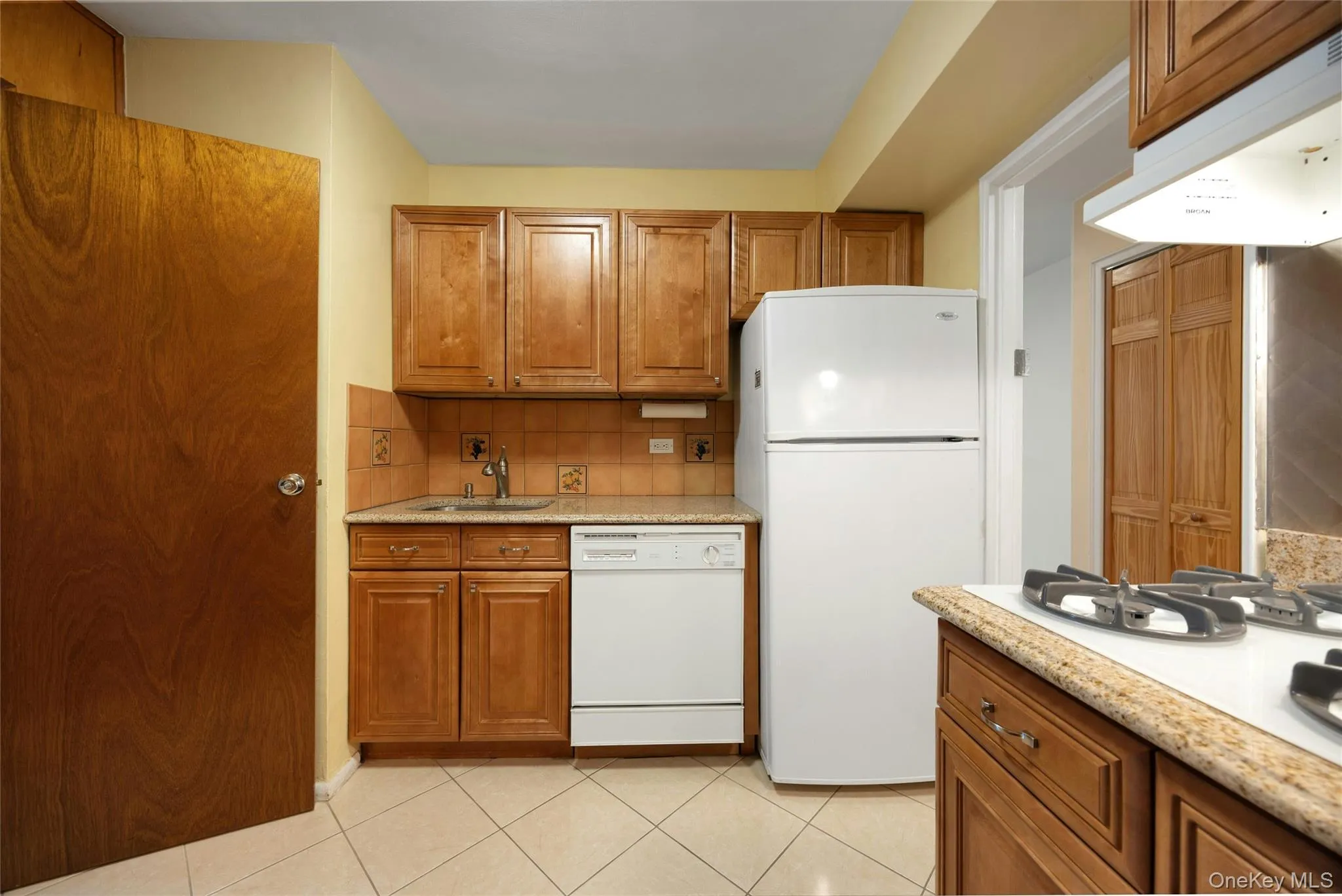 Kitchen featuring wood cabinetry, white appliances, and tiled flooring Kitchen featuring wood cabinetry, white appliances, and tiled flooring