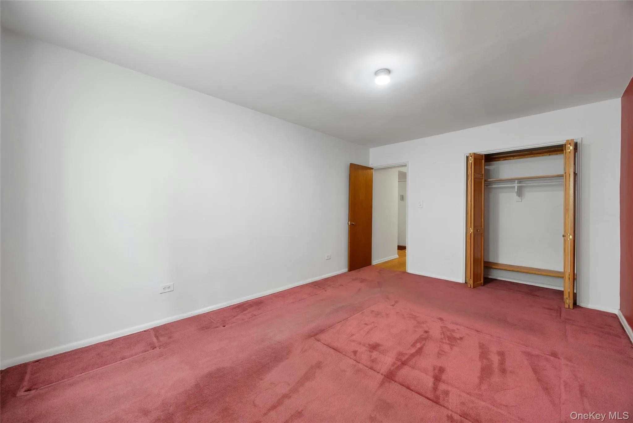 Spacious room featuring carpeting, white walls, a single ceiling light fixture, bi-fold closet doors, and wood-finish interior doors Spacious room featuring carpeting, white walls, a single ceiling light fixture, bi-fold closet doors, and wood-finish interior doors