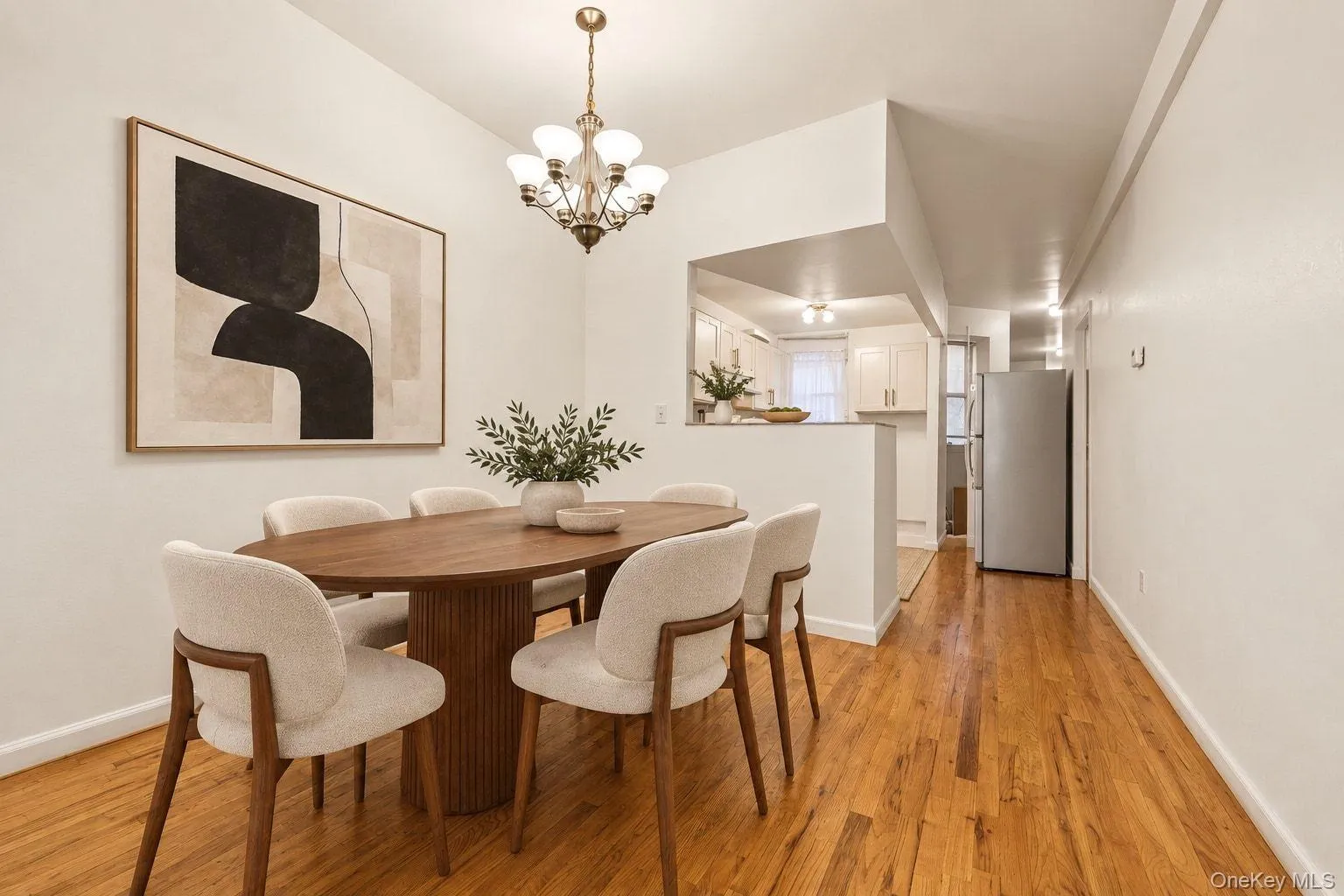 Hardwood flooring throughout, with a recessed kitchen area featuring white cabinetry and a built-in refrigerator Hardwood flooring throughout, with a recessed kitchen area featuring white cabinetry and a built-in refrigerator