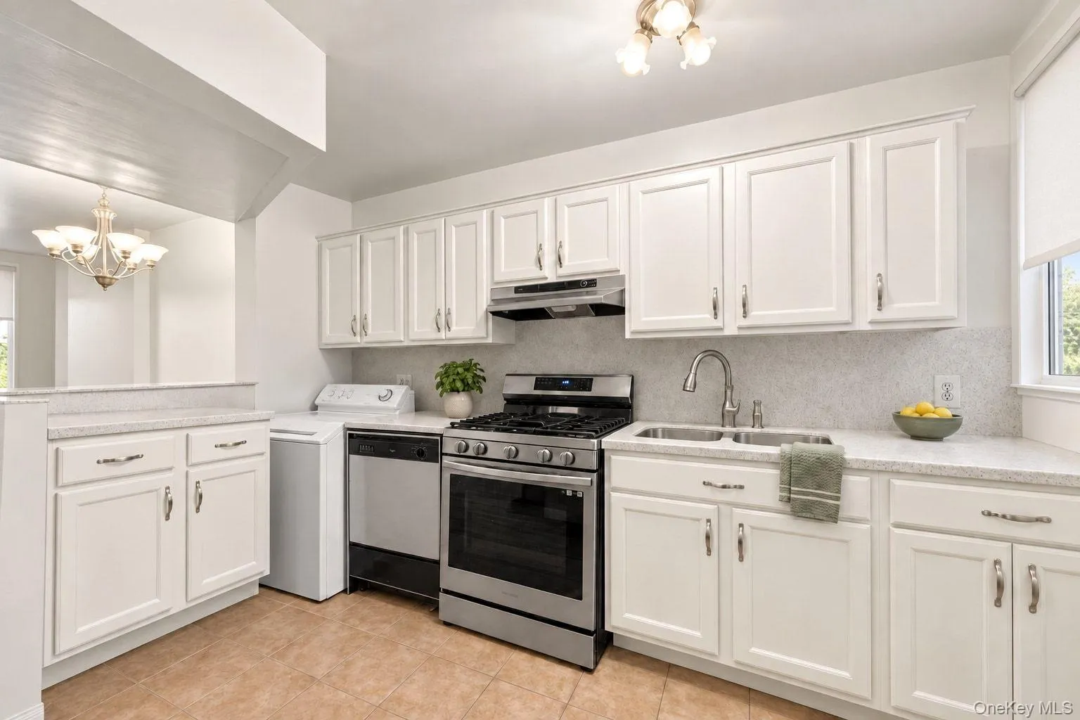 Kitchen featuring white cabinetry, light-toned countertops, a stainless steel gas range, a double basin sink, and tile flooring Kitchen featuring white cabinetry, light-toned countertops, a stainless steel gas range, a double basin sink, and tile flooring