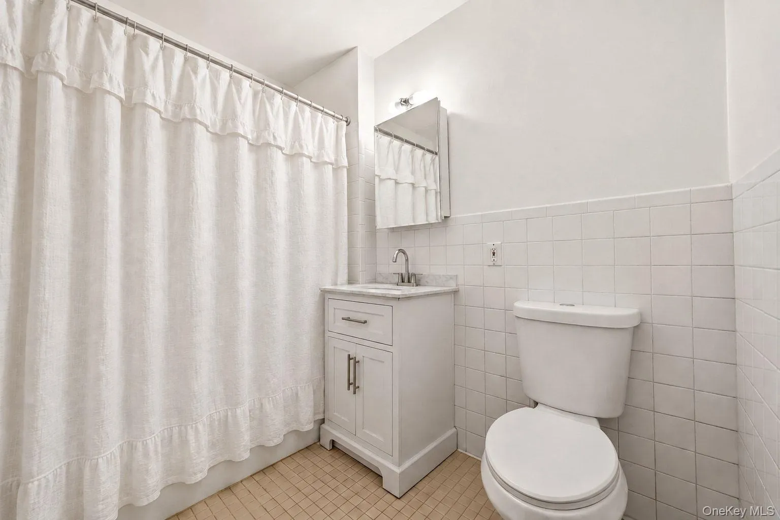 White tile wainscoting with a matching toilet, white vanity with a marble-finish countertop, and a recessed medicine cabinet White tile wainscoting with a matching toilet, white vanity with a marble-finish countertop, and a recessed medicine cabinet