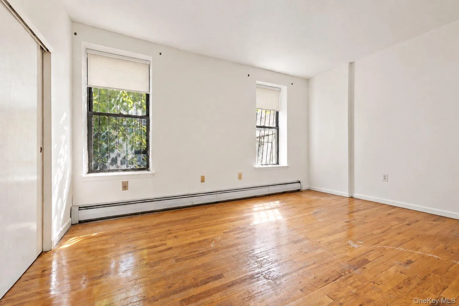 Hardwood flooring, two windows with roller shades, white walls, and a sliding closet door Hardwood flooring, two windows with roller shades, white walls, and a sliding closet door