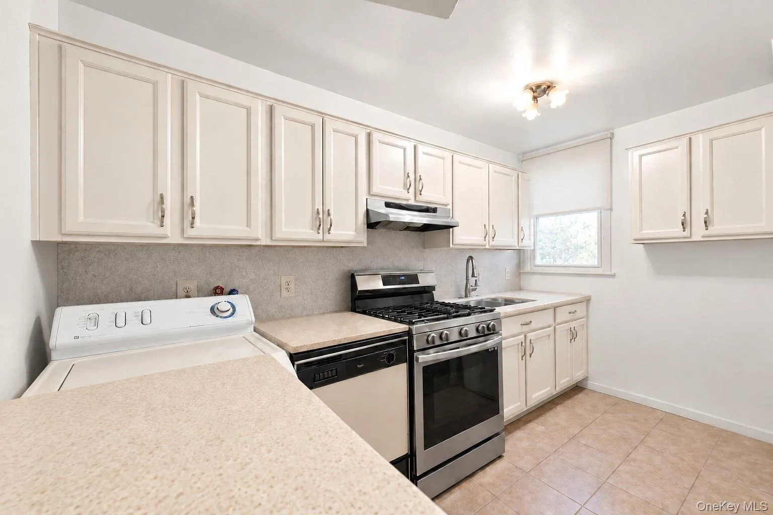 Kitchen featuring light-toned cabinetry, stainless steel appliances, a window with a roller shade, and tiled flooring Kitchen featuring light-toned cabinetry, stainless steel appliances, a window with a roller shade, and tiled flooring