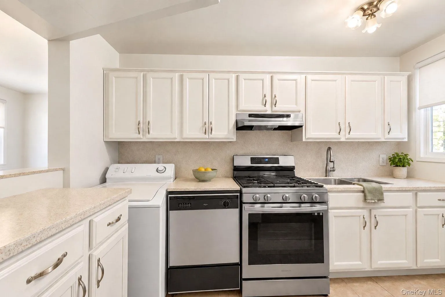 White cabinetry with brushed nickel hardware, light-toned countertops, stainless steel appliances, and a tile backsplash White cabinetry with brushed nickel hardware, light-toned countertops, stainless steel appliances, and a tile backsplash