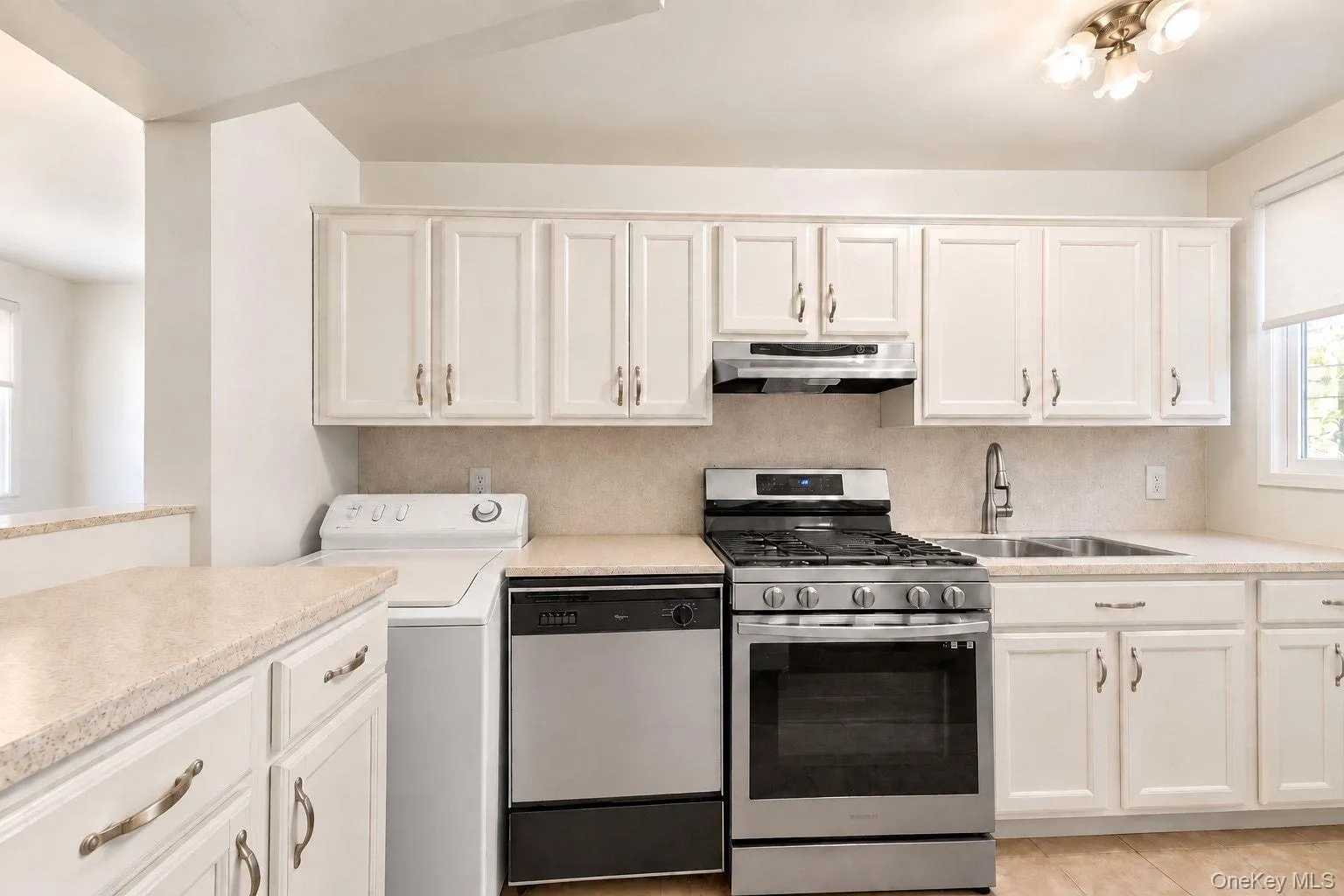 Kitchen featuring white cabinetry, light-toned countertops, a stainless steel gas range, a stainless steel dishwasher, and a double basin sink Kitchen featuring white cabinetry, light-toned countertops, a stainless steel gas range, a stainless steel dishwasher, and a double basin sink