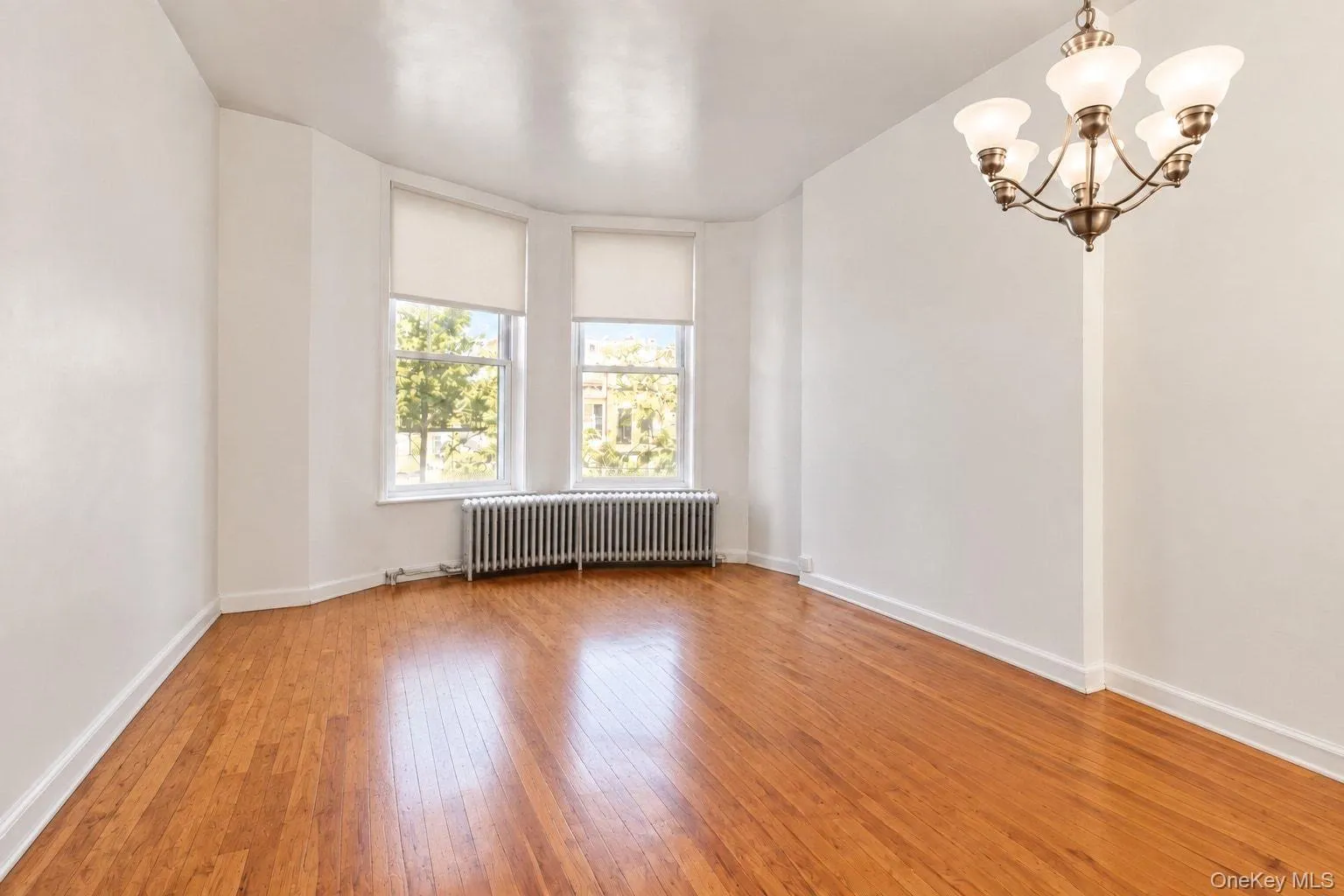 Hardwood flooring, bay window with two windows, built-in radiator, and a five-light chandelier Hardwood flooring, bay window with two windows, built-in radiator, and a five-light chandelier
