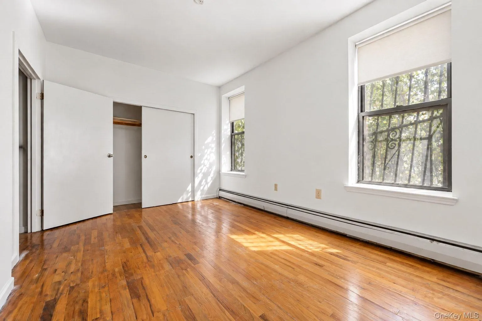 Hardwood flooring, two windows with security bars, white walls, and a built-in closet with sliding doors Hardwood flooring, two windows with security bars, white walls, and a built-in closet with sliding doors