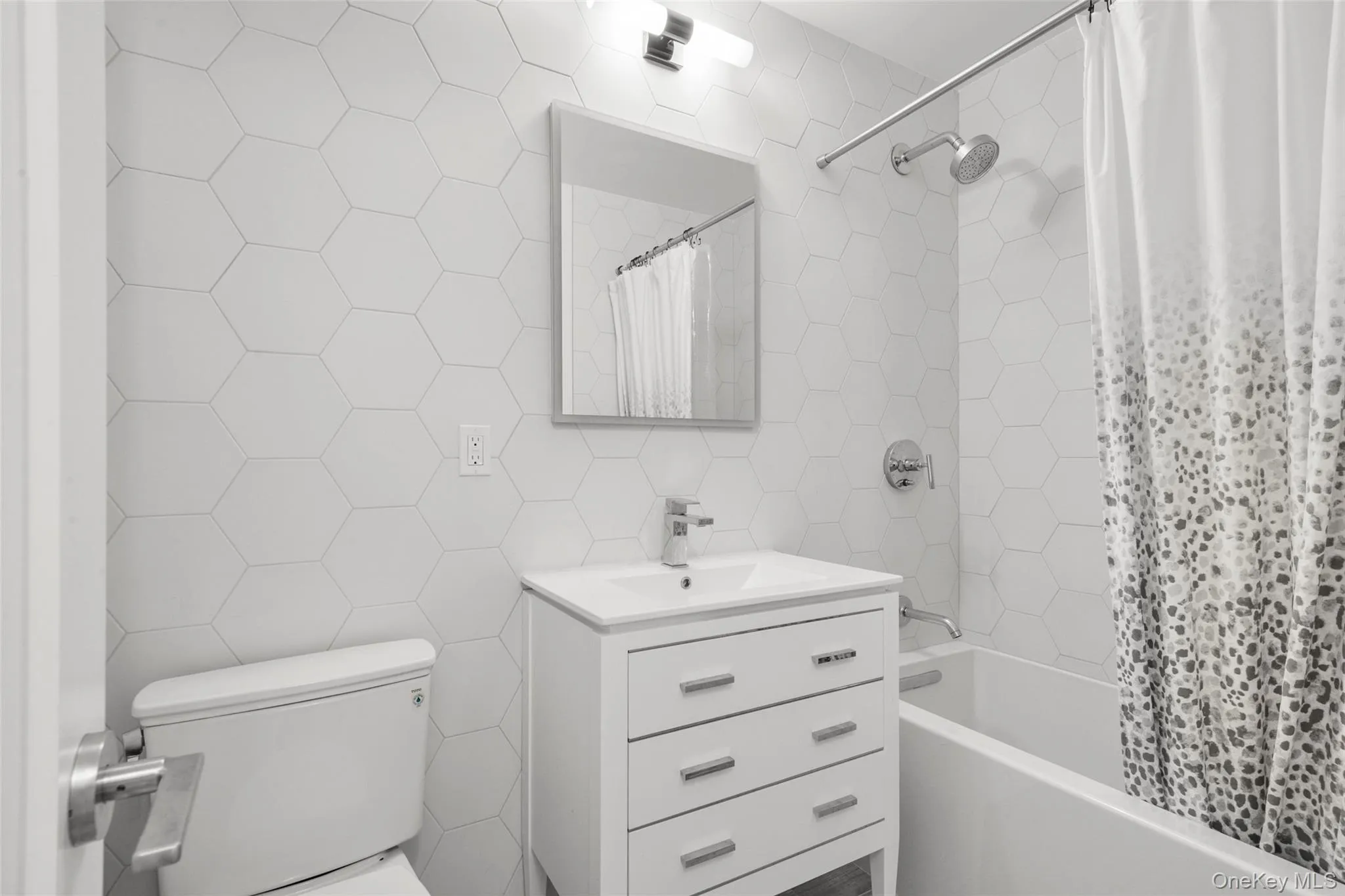 Bathroom featuring hexagon wall tiling, white vanity with integrated sink, full bathtub Bathroom featuring hexagon wall tiling, white vanity with integrated sink, full bathtub