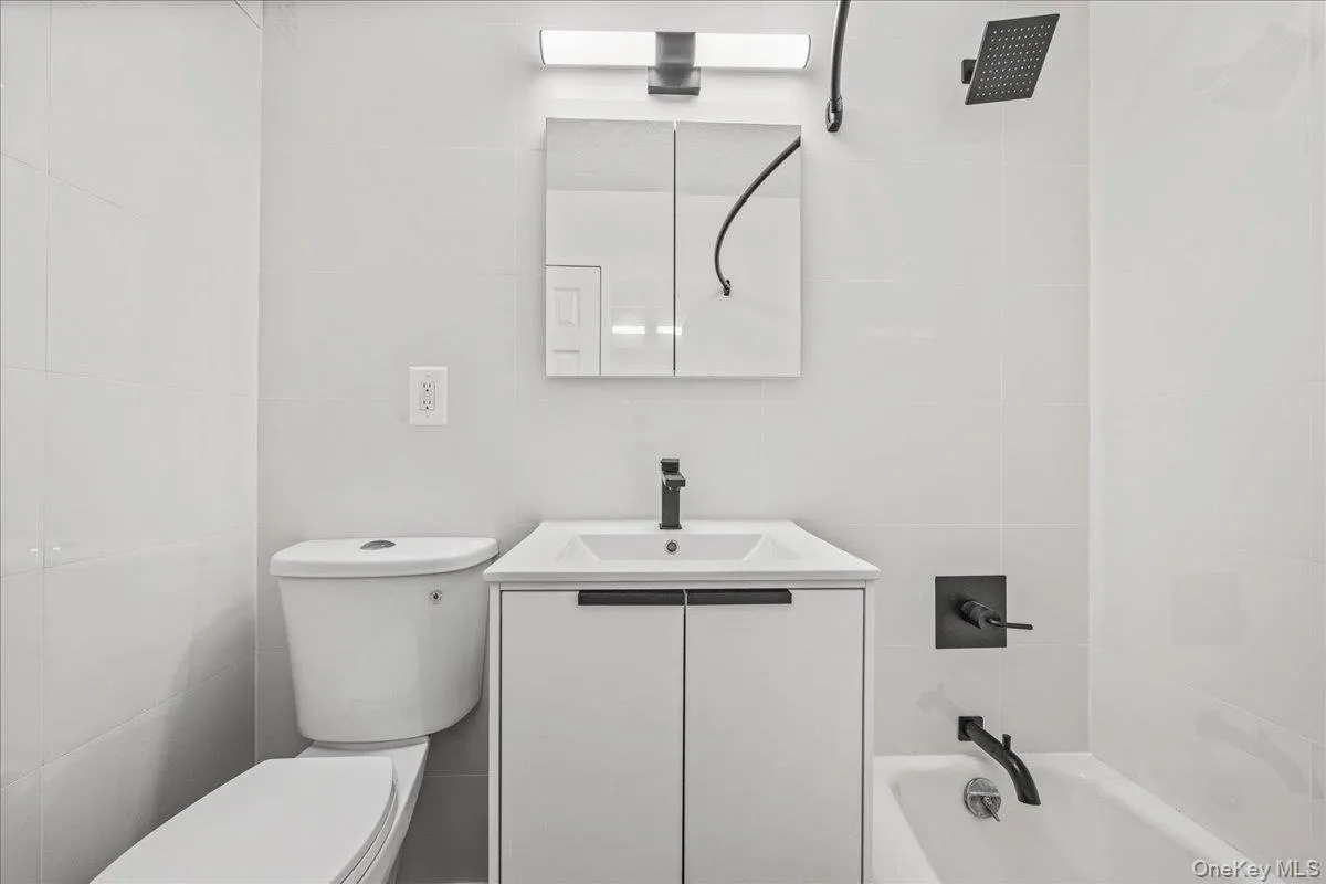 White tiled shower surround, modern vanity with integrated sink, black matte fixtures, rectangular medicine cabinet, and contemporary overhead lighting White tiled shower surround, modern vanity with integrated sink, black matte fixtures, rectangular medicine cabinet, and contemporary overhead lighting