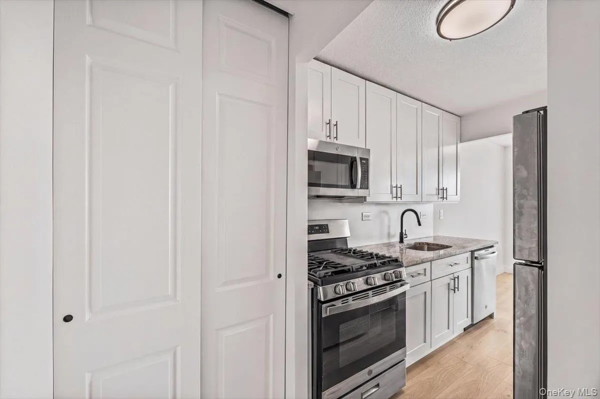 Kitchen featuring white shaker cabinetry, stainless steel appliances, granite countertops, and vinyl flooring Kitchen featuring white shaker cabinetry, stainless steel appliances, granite countertops, and vinyl flooring