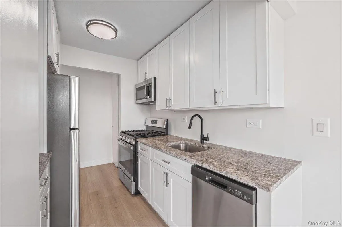 White cabinetry, stainless steel appliances, vinyl flooring, stone countertops, and a matte black faucet White cabinetry, stainless steel appliances, vinyl flooring, stone countertops, and a matte black faucet