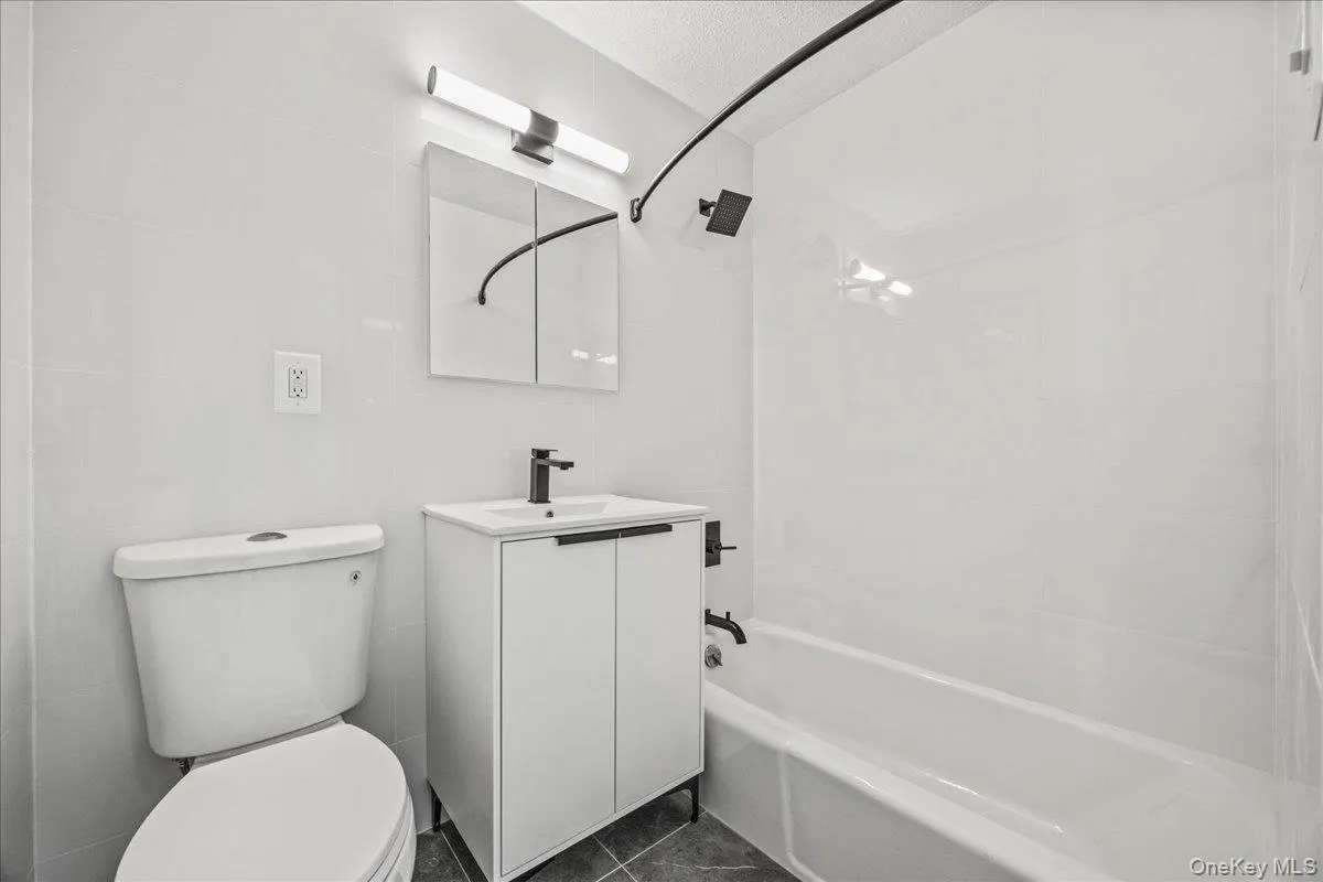 White subway tile shower surround, modern vanity with white countertop, wall-mounted medicine cabinet, sleek black fixtures, and dark floor tiling White subway tile shower surround, modern vanity with white countertop, wall-mounted medicine cabinet, sleek black fixtures, and dark floor tiling