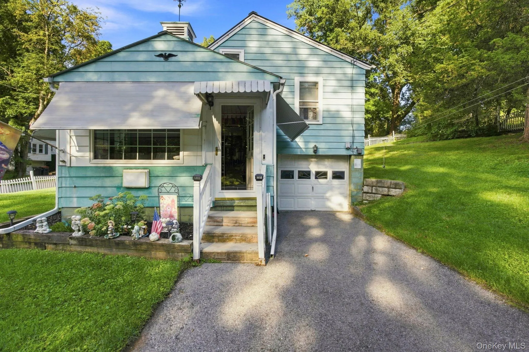 Turquoise siding exterior with white trim, featuring a white metal awning over the entry door and a single-car garage Turquoise siding exterior with white trim, featuring a white metal awning over the entry door and a single-car garage